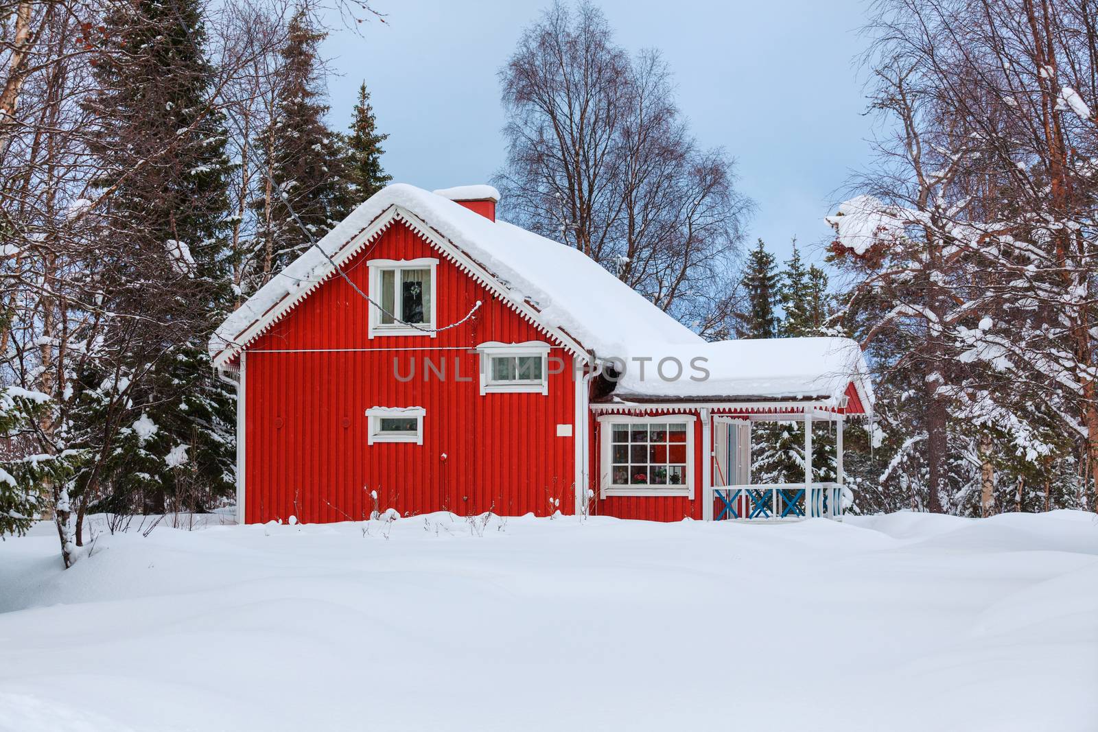 Red wooden Finnish house in winter forest covered with snow