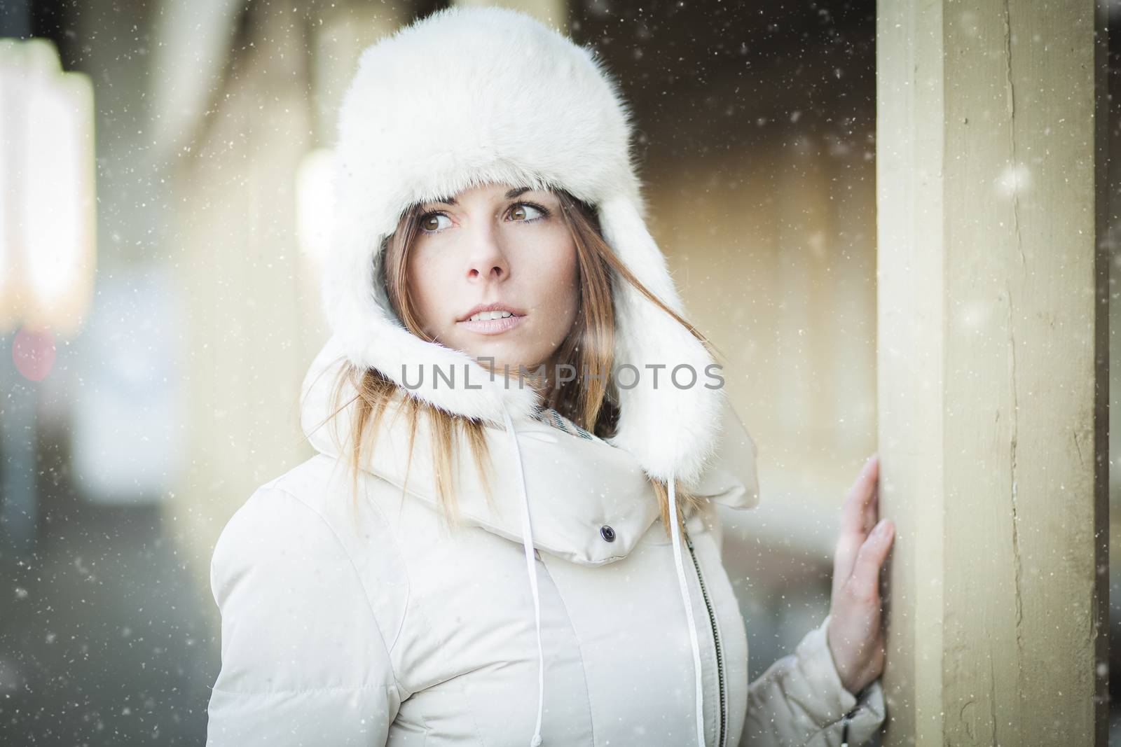 Young woman in fur hat and down jacket under falling snow