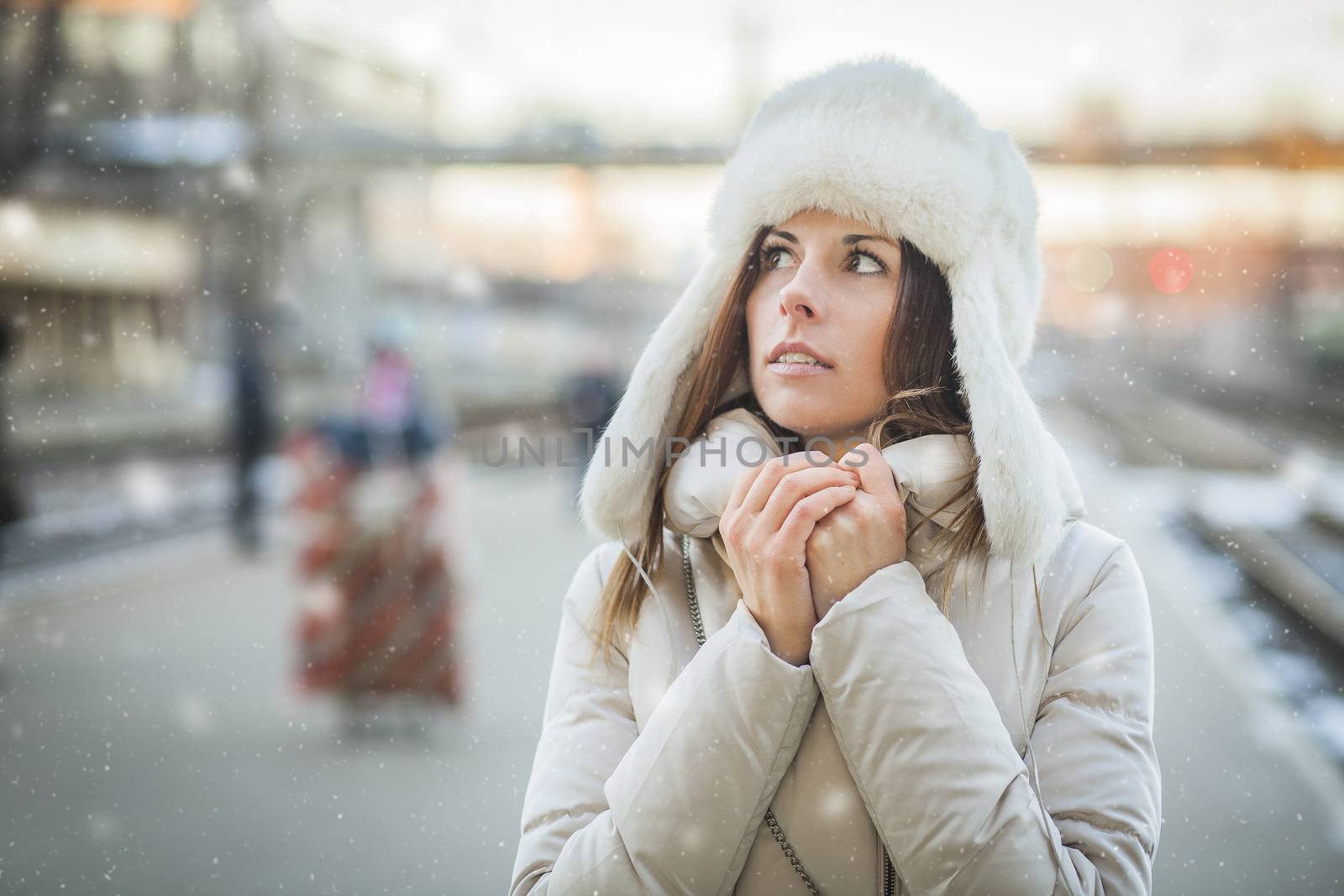 Girl is trying to warm up on a railroad station in snowy day