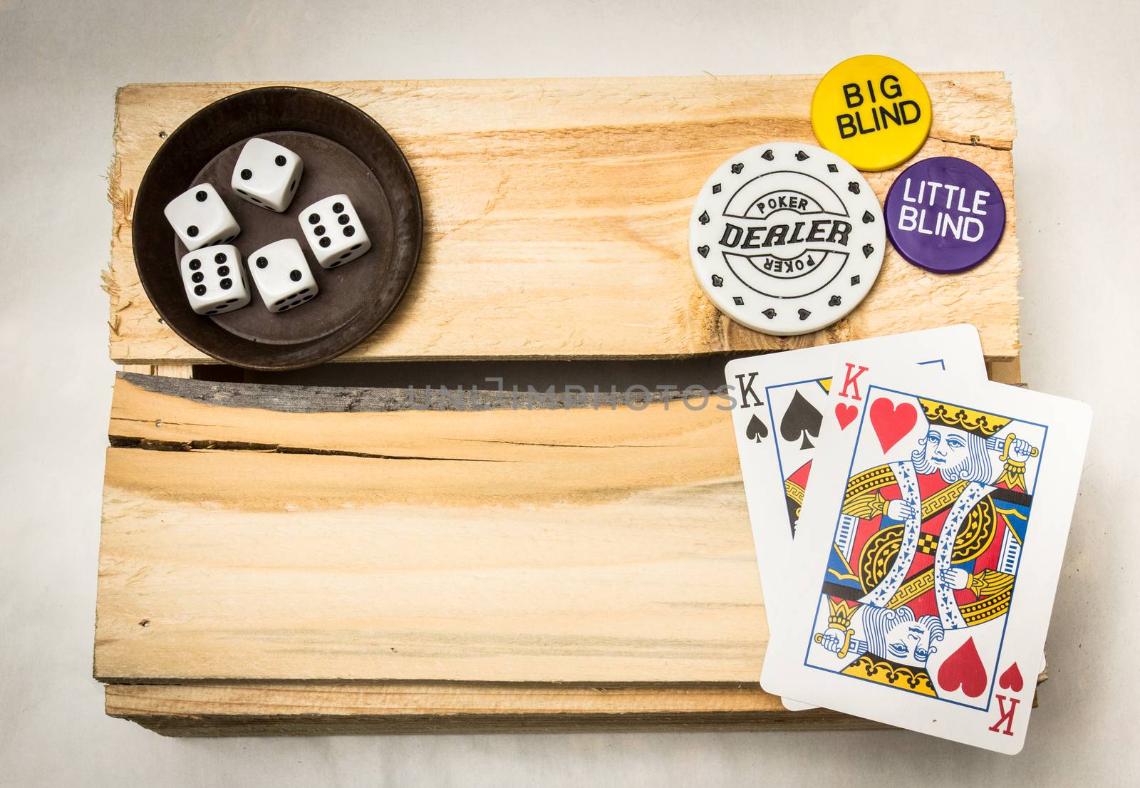 A pair of kings together with dices and a dealer button on a wooden support