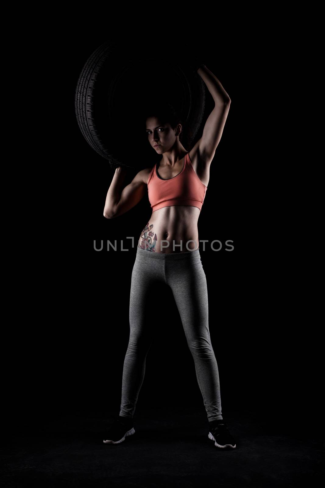 fitness girl lifting a tyre, against black background