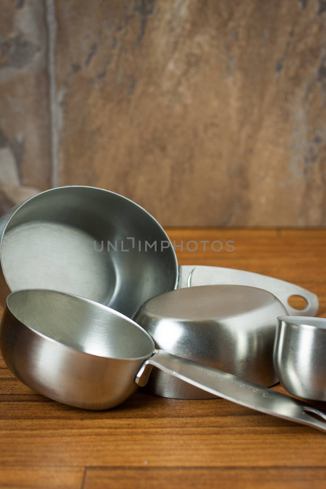 Aluminum measuring spoons sitting on a wooden surface.