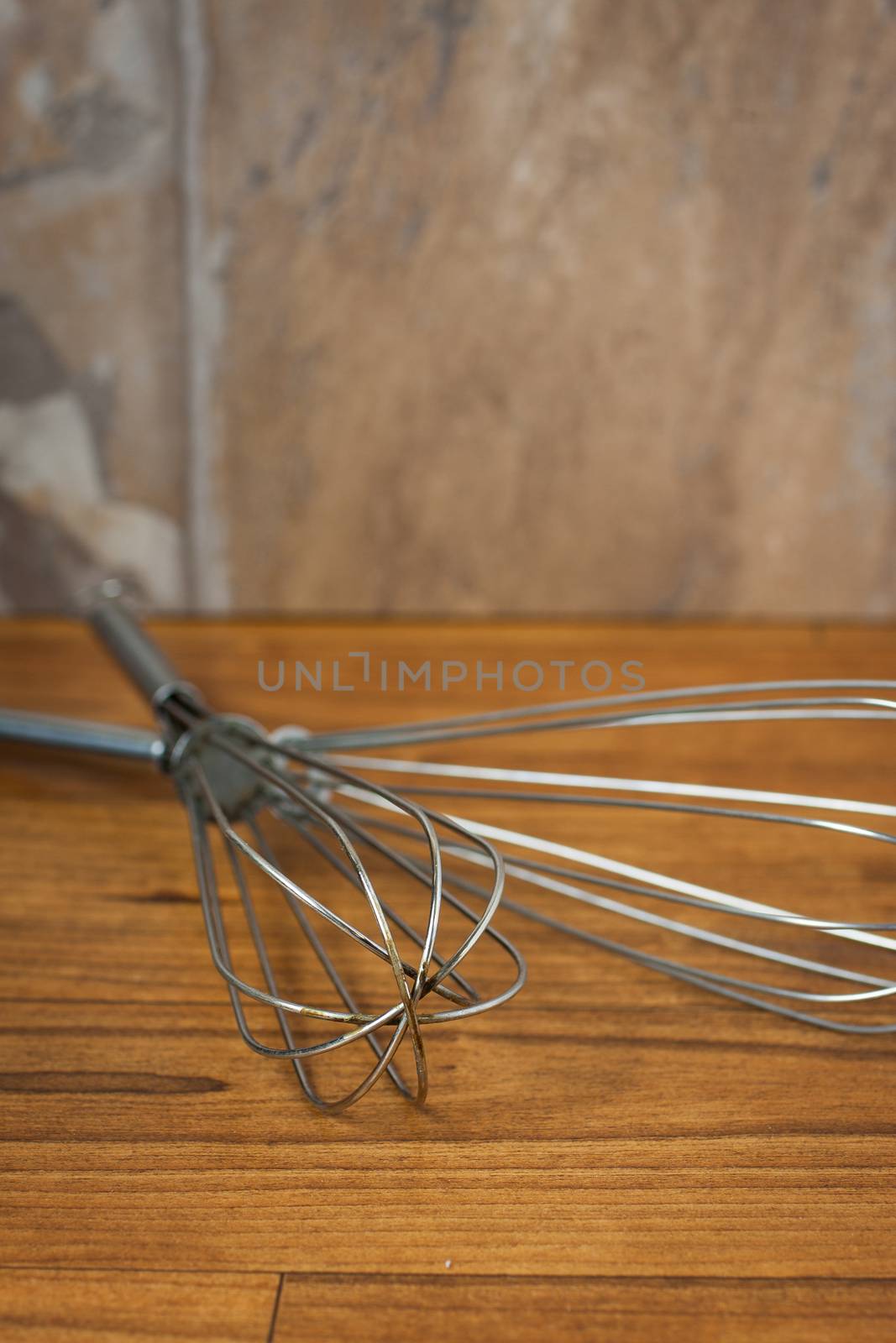 Well used metal wisks lay on a wooden counter.