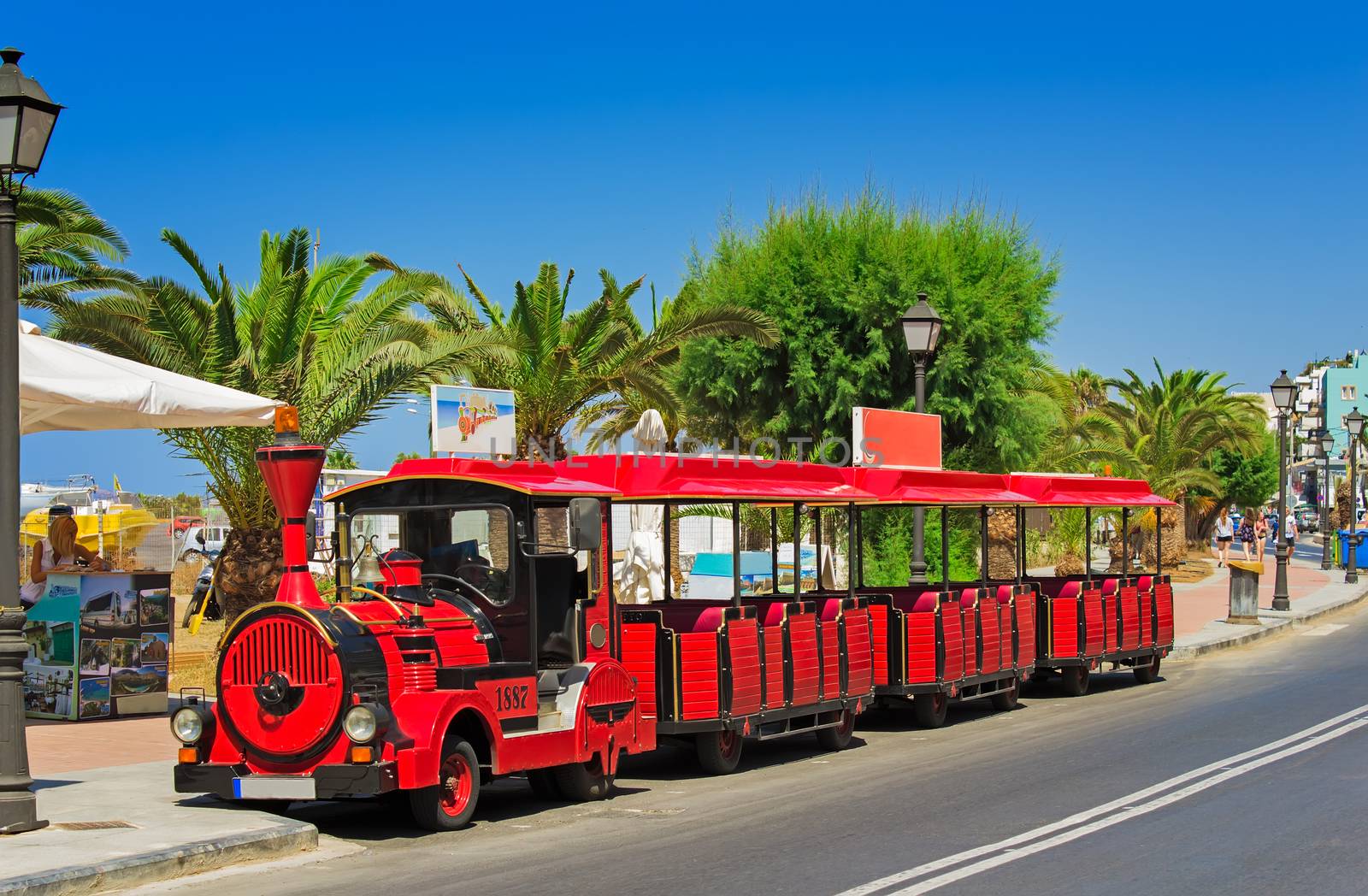 Bright red car in the style of an old steam train with open cars in the resort town for the transportation of tourists.