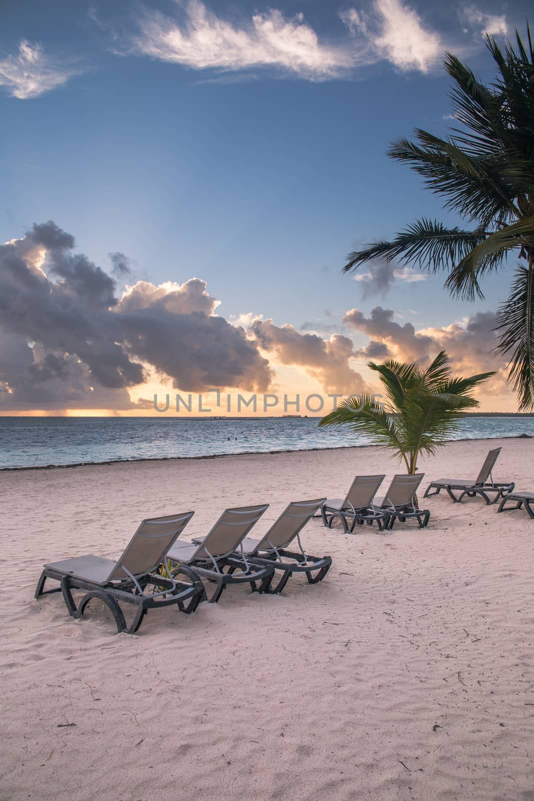 Sunrise on a Caribbean beach with sunbeds and palm trees