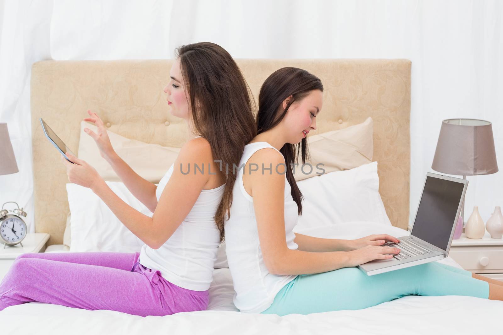 Pretty friends using their technology on bed at home in the bedroom