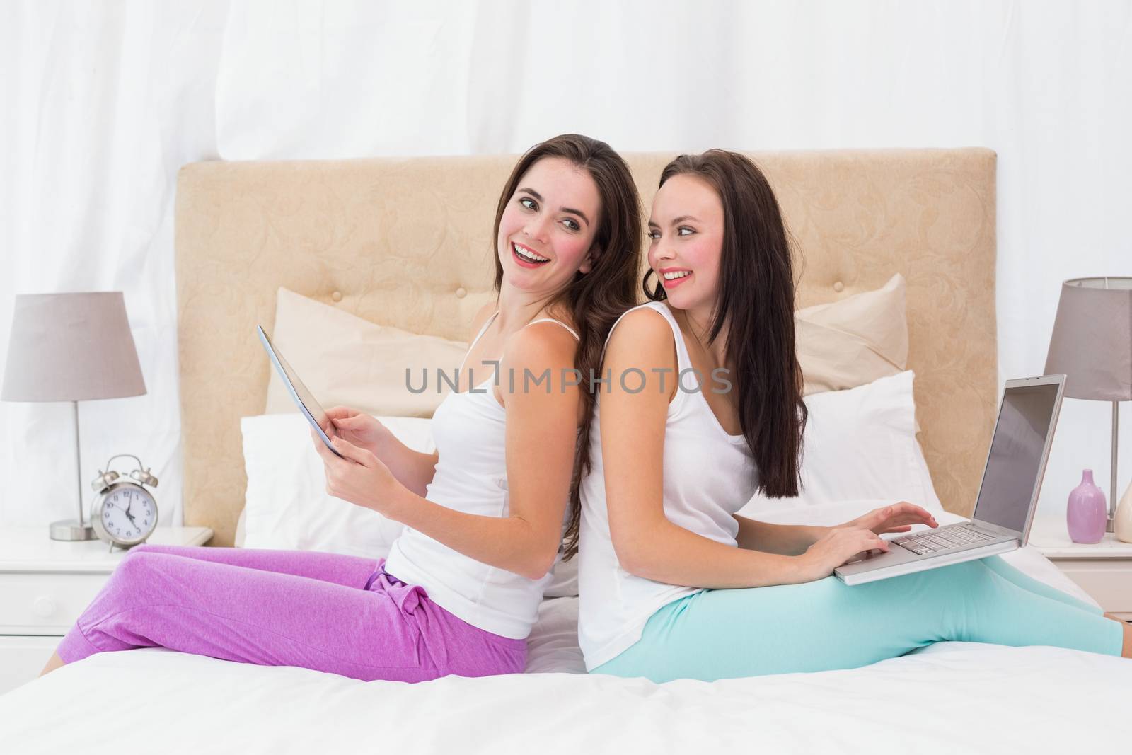 Pretty friends using their technology on bed by Wavebreakmedia