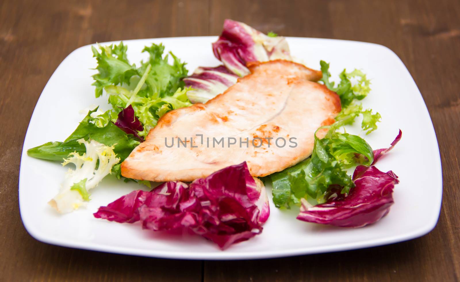 Chicken and salad on plate on wooden table