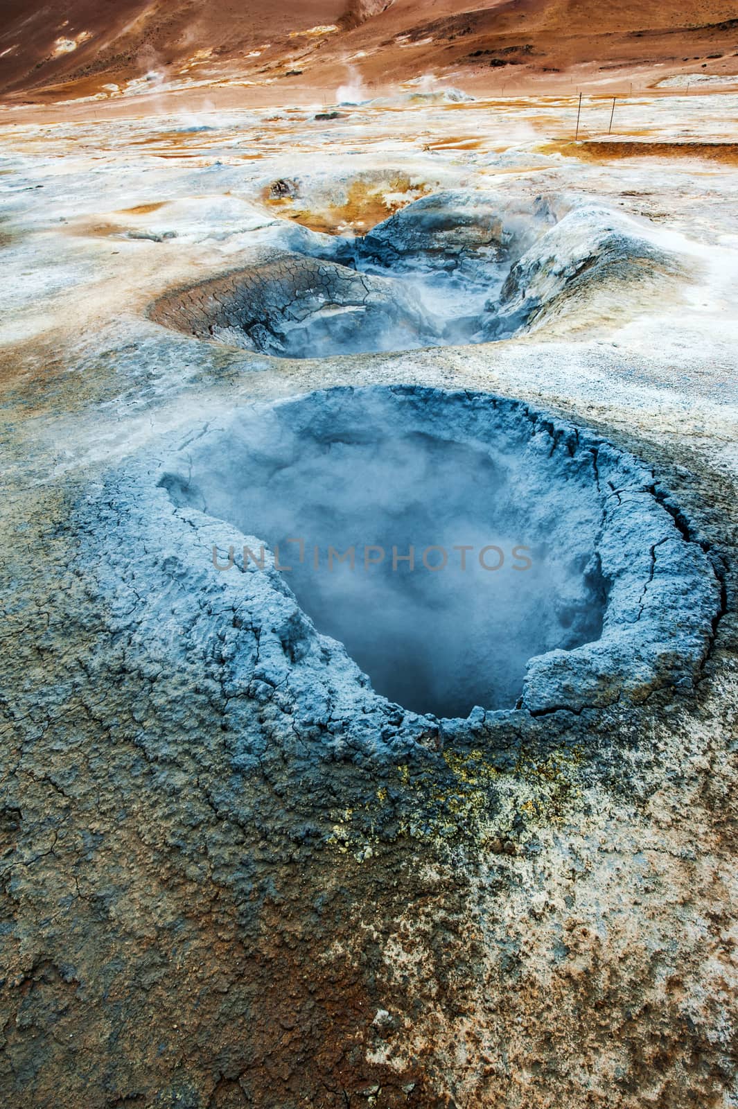 Mudpot in the geothermal area Hverir, Iceland. The area around the boiling mud is multicolored and cracked. 