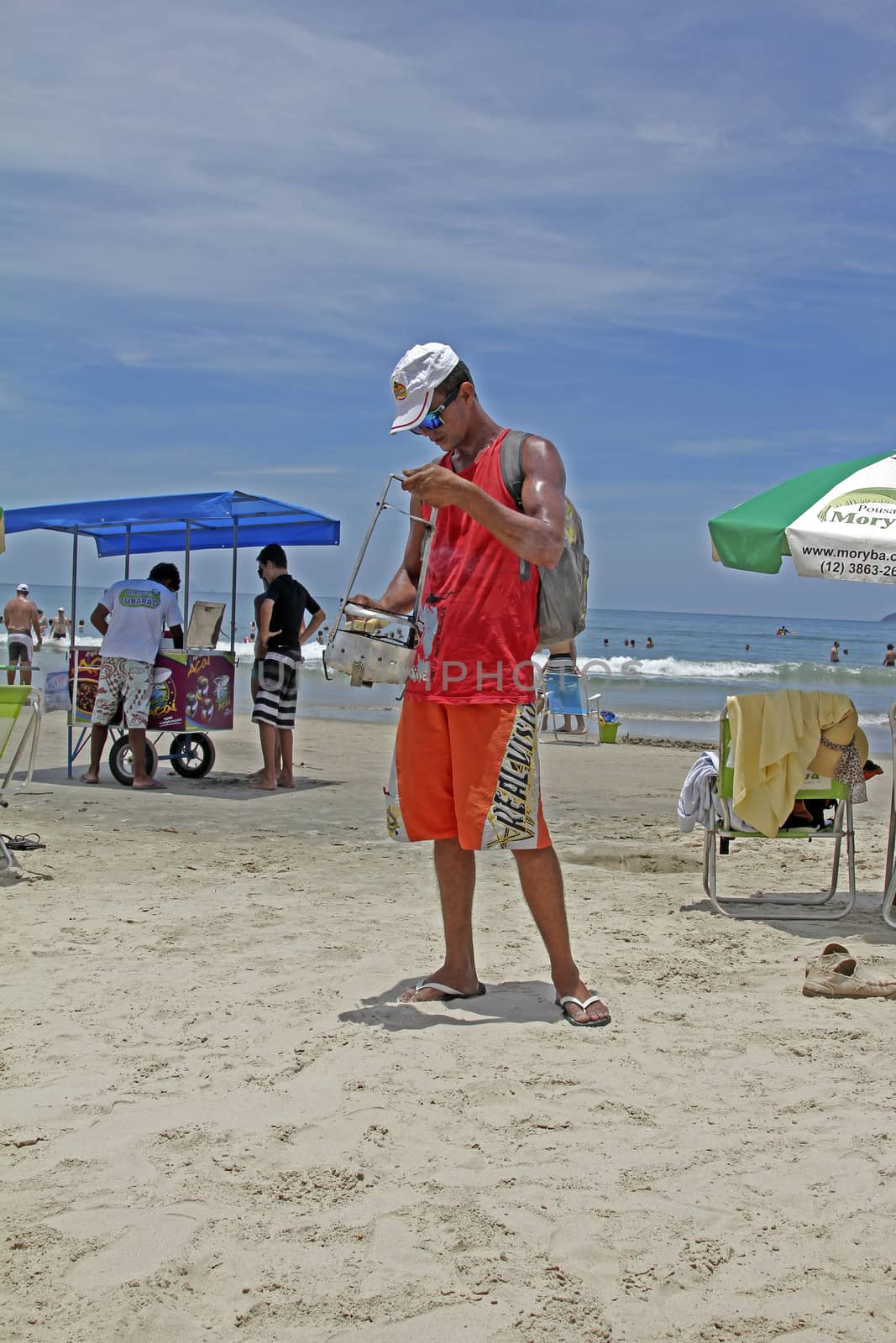 SAO SEBASTIAO, BRAZIL - JANUARY 04, 2015: An unidentified walking vendor with hand-held charcoal oven roasting handmade cheese on a beach in Brazil.