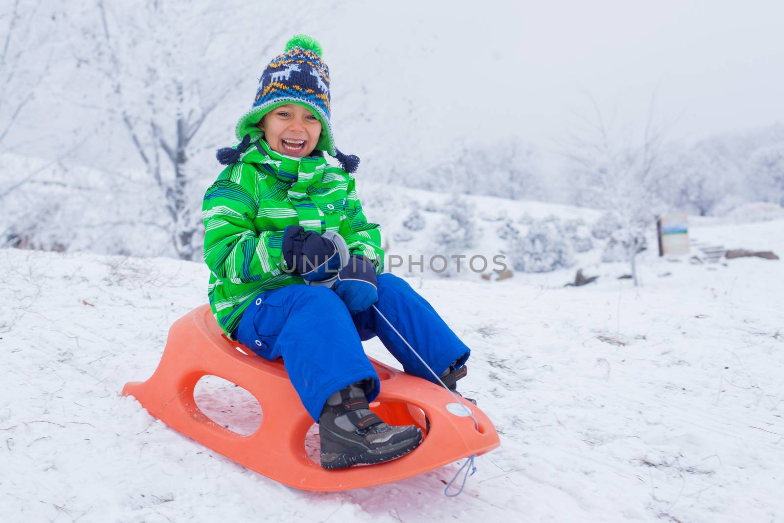 Little boy having fun with sled in winter park by maxoliki