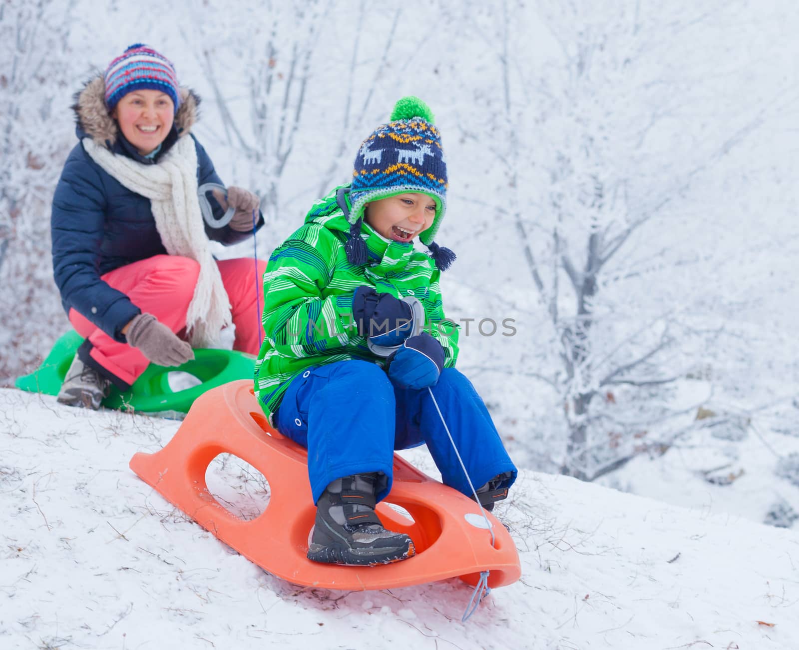 Winter, play, fun - Cute little boy and his mother having fun with sled in winter park