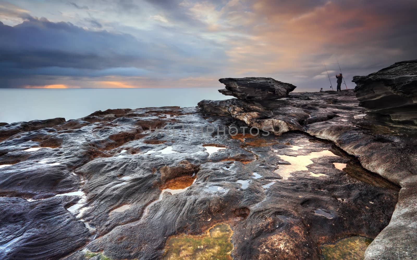 The view south from South Curl Curl rocks, NSW Australia.   The rock really grabbed my eye and this was where the most colour concentration from sunrise was warming up the stormy clouds.  A fisherman clenches fists in jubilation.
