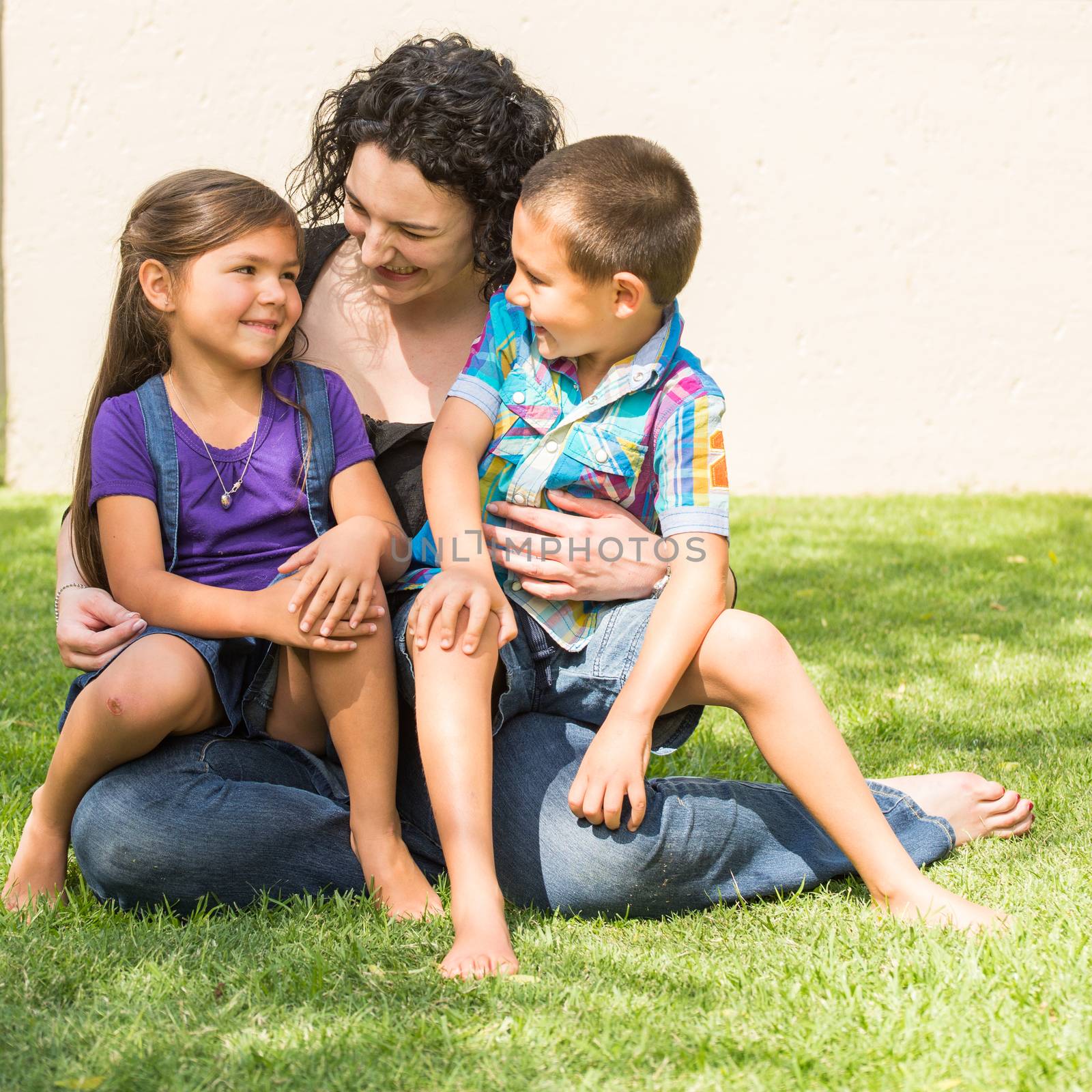 Mother, daughter, and son outside in the garden sitting together on the lawn on summer day. All three interacting with each other.