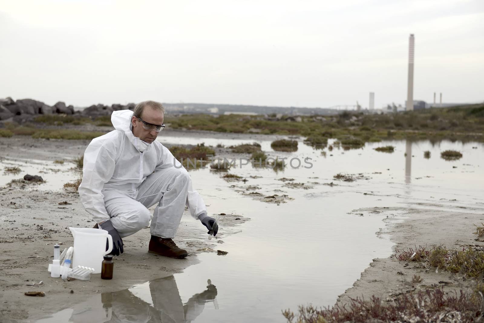 
Worker in a protective suit examining pollution in the water at the industry.