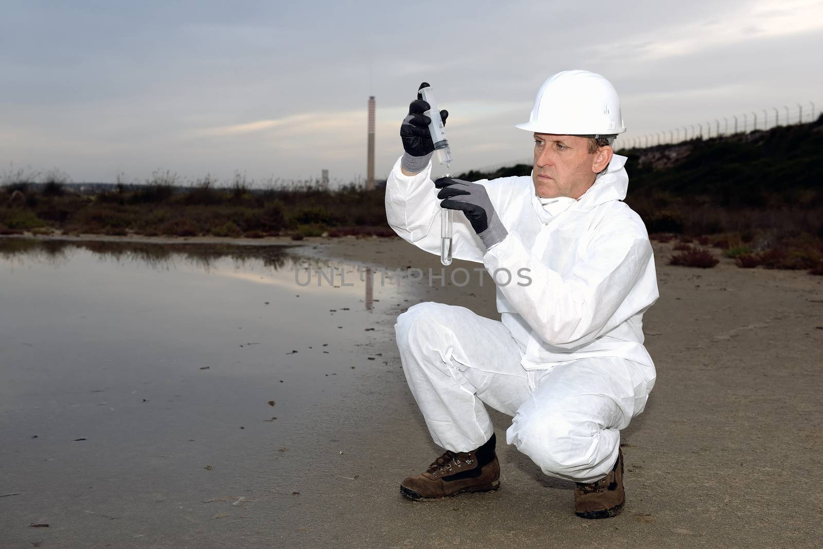 
Worker in a protective suit examining pollution in the water at the industry.
