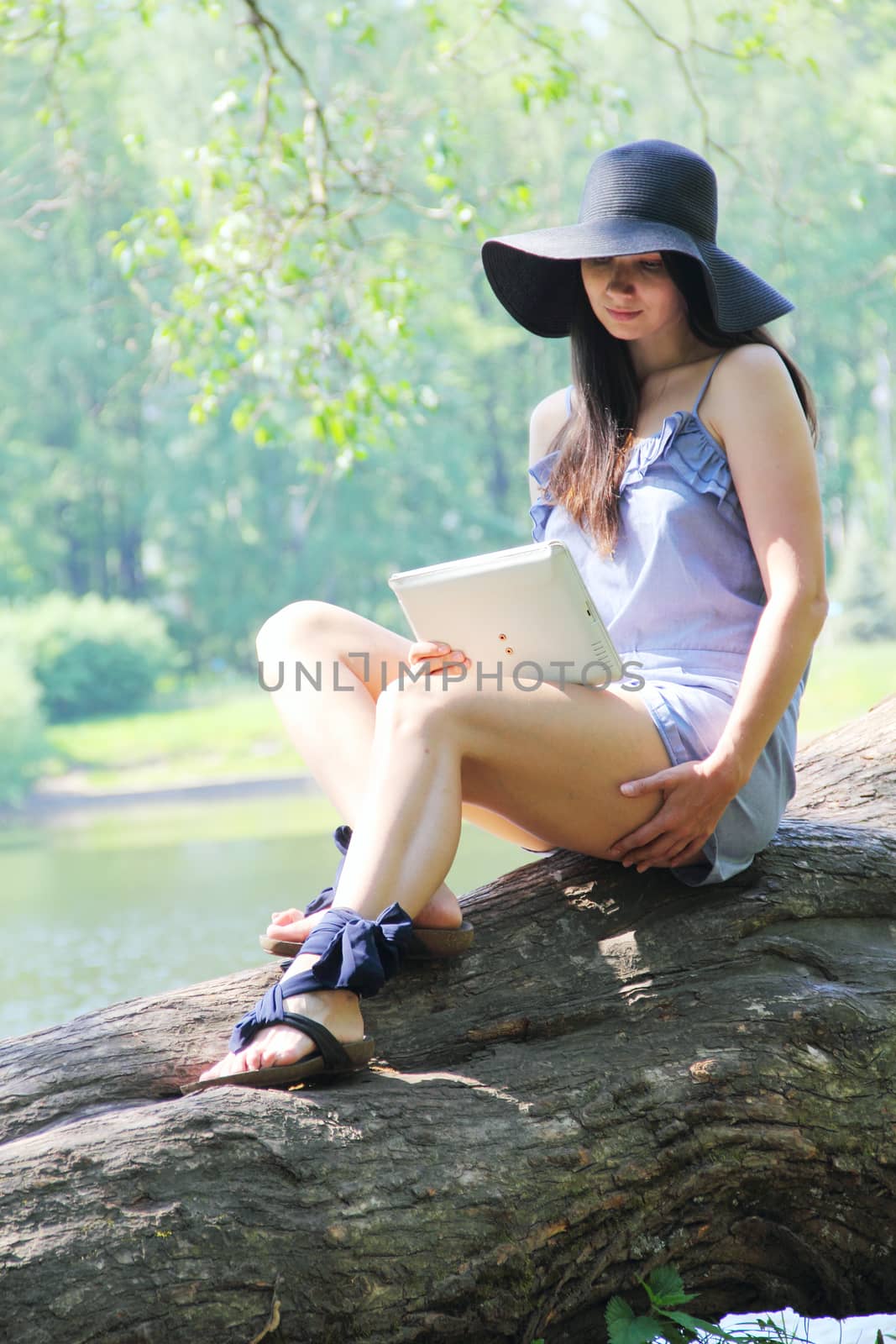 Young woman using tablet outdoor sitting on tree near lake