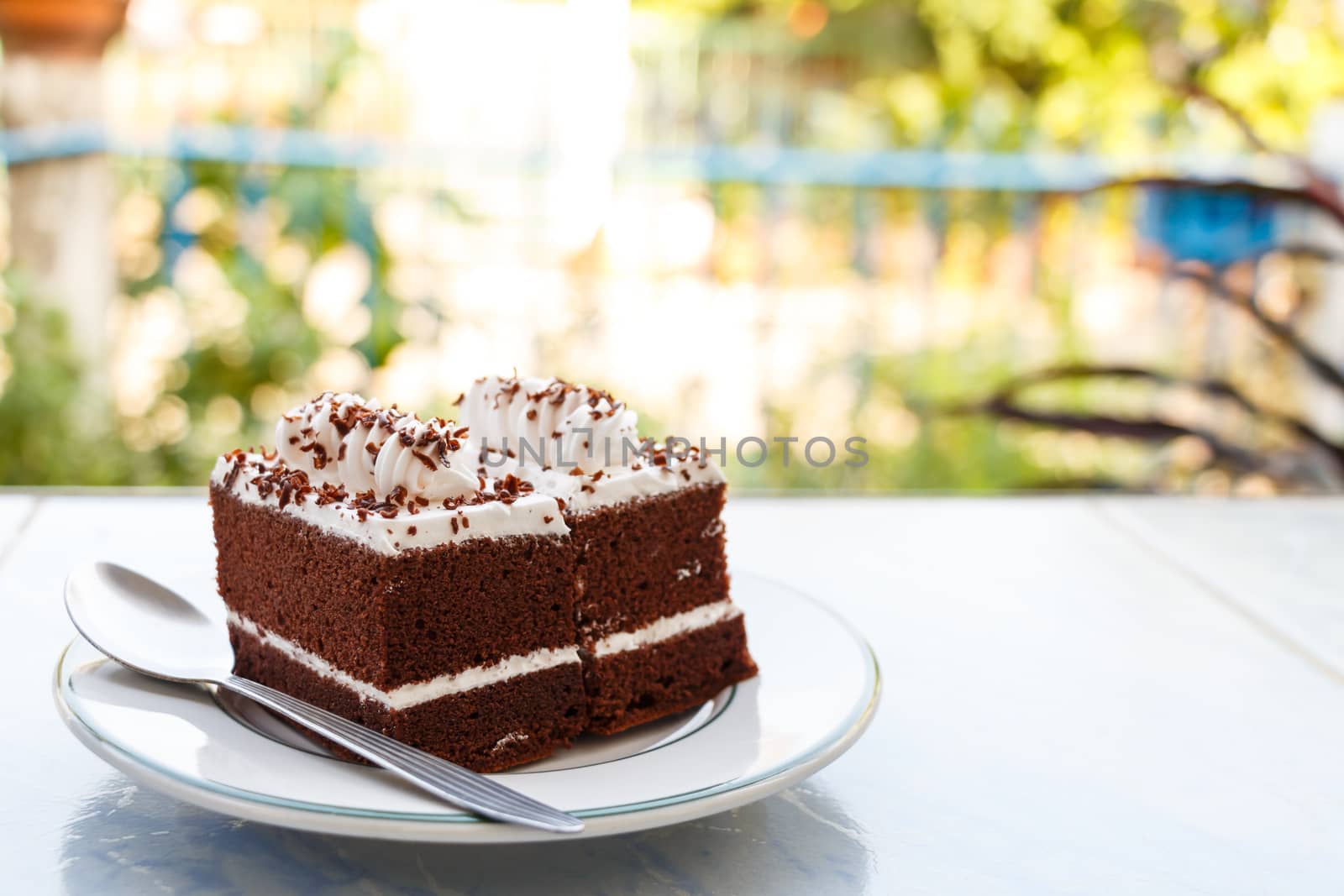 chocolate cakes with white cream on top and spoon on plate in house and plant at background