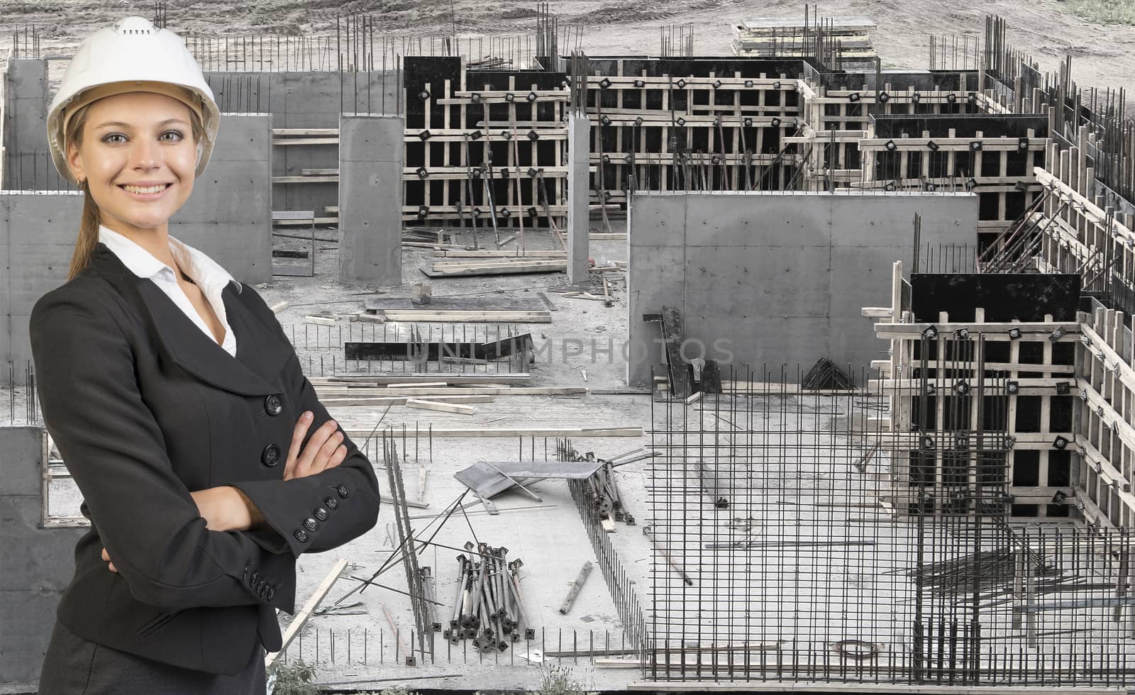 Beautiful businesswoman in helmet standing with crossed arms. Construction site as backdrop by cherezoff