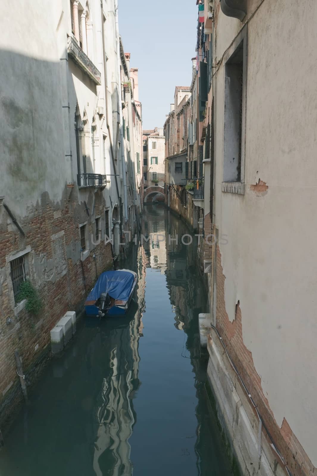 Narrow Venetian canal with a boat and reflections