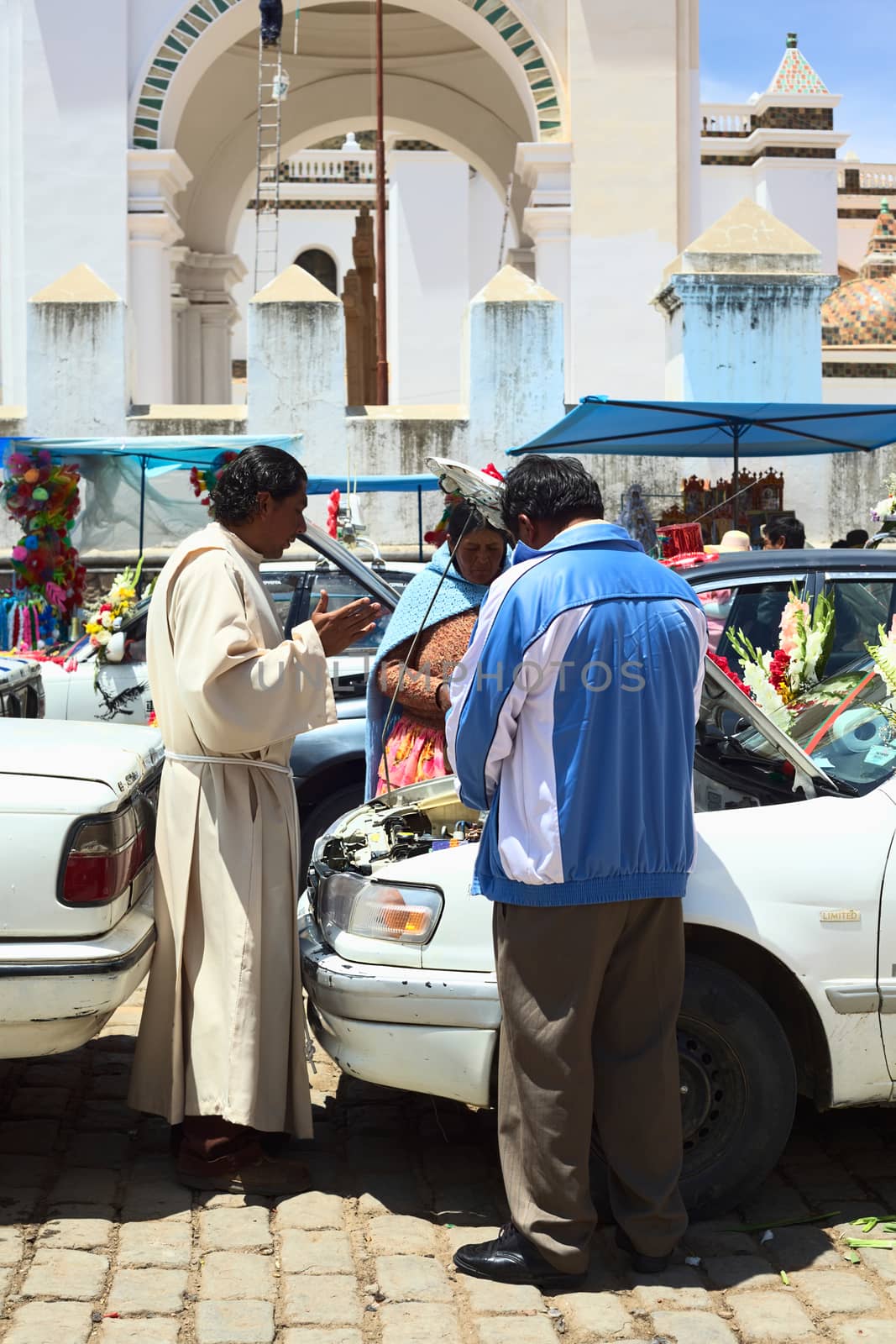 COPACABANA, BOLIVIA - OCTOBER 20, 2014: Priest saying a prayer in front of the open hood of a car at the blessing of vehicles on 6 de Agosto avenue outside the basilica in the small tourist town on October 20, 2014 in Copacabana, Bolivia. 