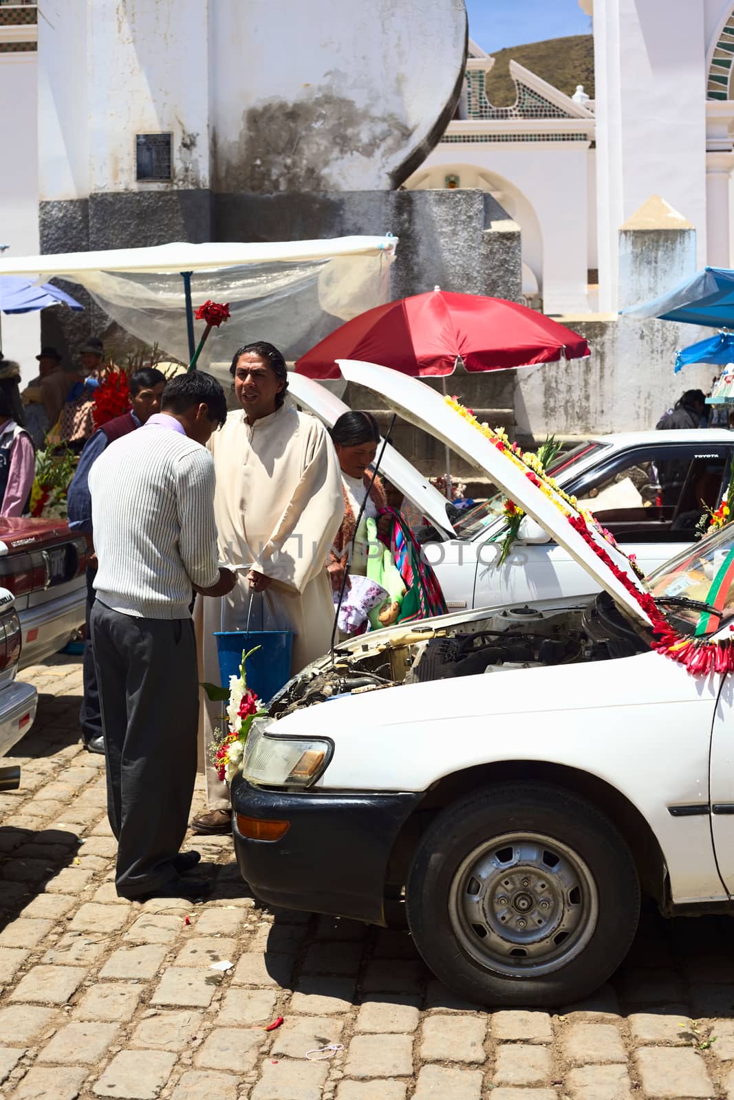 COPACABANA, BOLIVIA - OCTOBER 20, 2014: Unidentified priest blesses driver/owner of a car at the blessing of automobiles in front of the basilica on 6 de Agosto avenue in the center of the small tourist town on October 20, 2014 in Copacabana, Bolivia. Almost every day many cars, taxis, buses and vans are standing in line to receive blessing from a priest of the basilica.