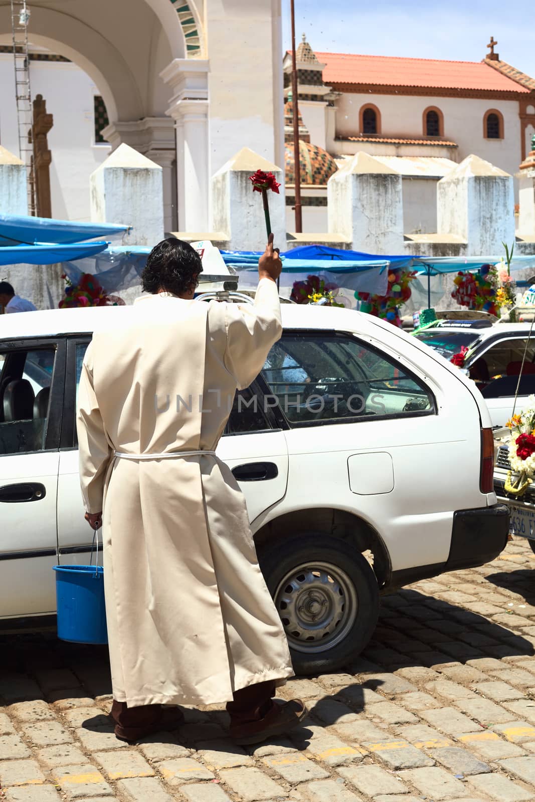 COPACABANA, BOLIVIA - OCTOBER 20, 2014: Unidentified priest sprinkling holy water on a car at the blessing of automobiles in front of the basilica on 6 de Agosto avenue in the center of the small tourist town on October 20, 2014 in Copacabana, Bolivia. Almost every day many cars, taxis, buses and vans are standing in line to receive blessing from a priest of the basilica.