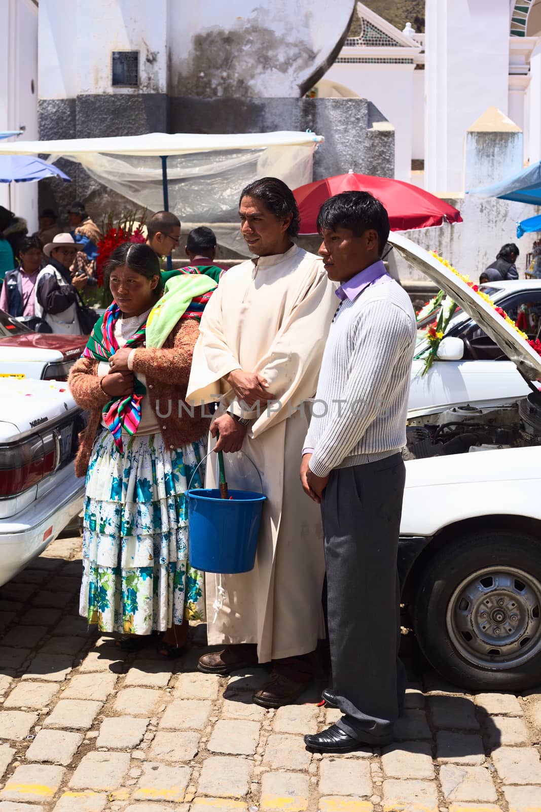 COPACABANA, BOLIVIA - OCTOBER 20, 2014: Unidentified priest with owners of a car posing for a photograph at the blessing of vehicles in front of the basilica on 6 de Agosto avenue in the center on October 20, 2014 in Copacabana, Bolivia. The blessing of automobiles takes place daily and is a ritual attended by many.