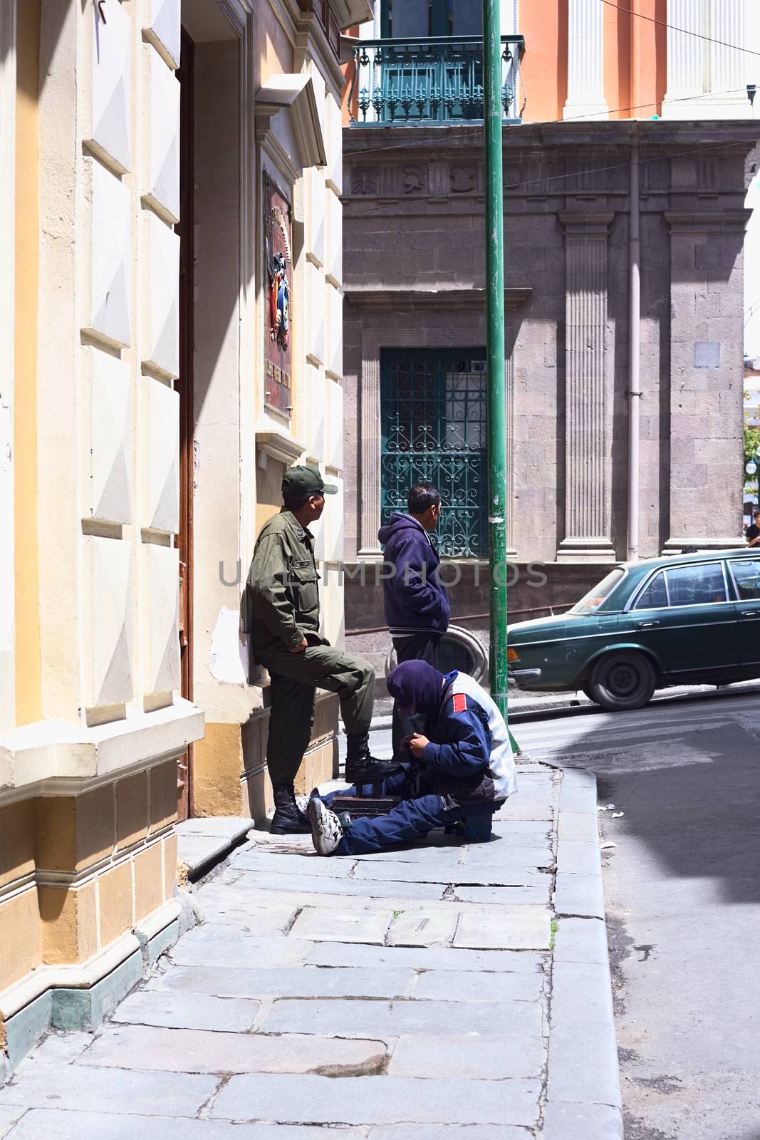 LA PAZ, BOLIVIA - OCTOBER 11, 2014: Unidentified shoeblack cleaning the boots of a man in uniform at the corner of the streets Bolivar and Comercio in the city center on Octobr 11, 2014 in La Paz, Bolivia