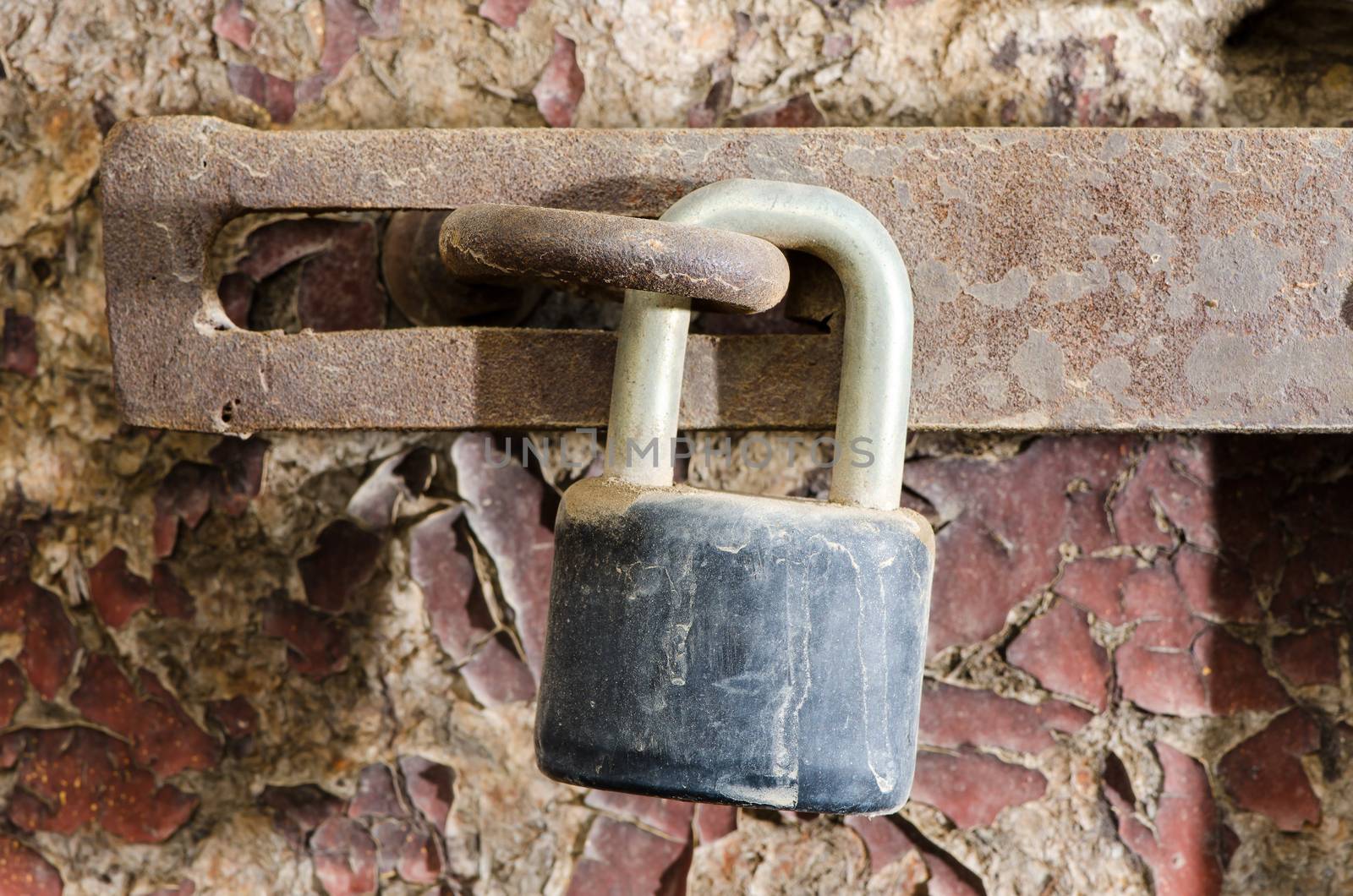 Old rusty padlock on damaged wooden doors surface.