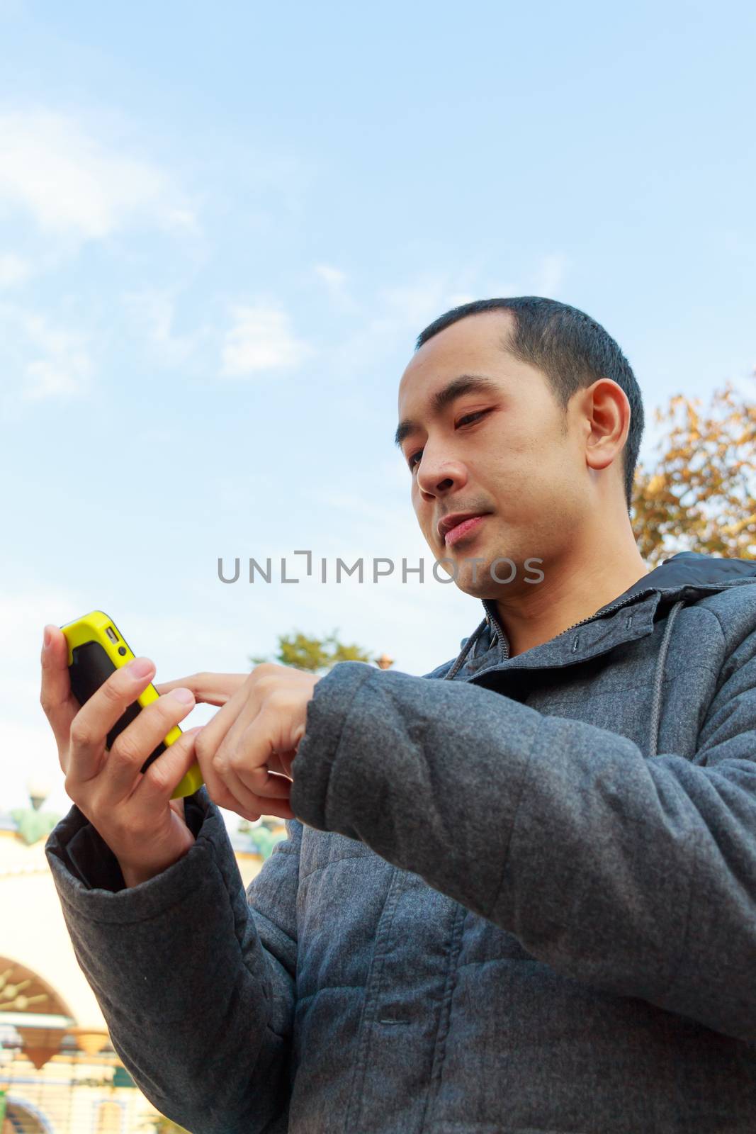 handsome thai man with gray coat is playing mobile phone