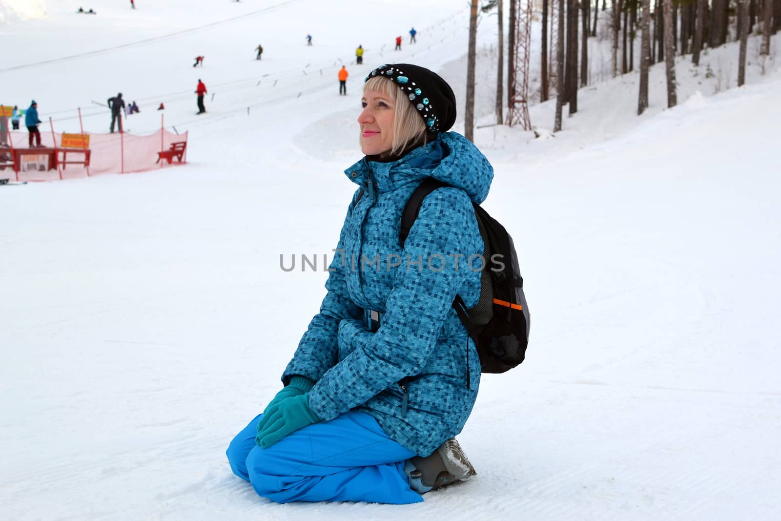 The woman in winter clothes sits on snow against the ski slope. by veronka72