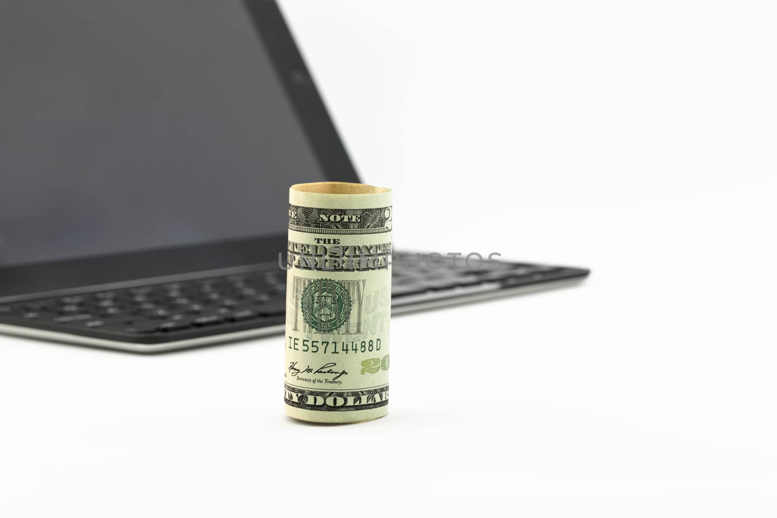 Focus on American dollar standing upright in front of tablet and keyboard.  Selective focus on money with copy space to right. 