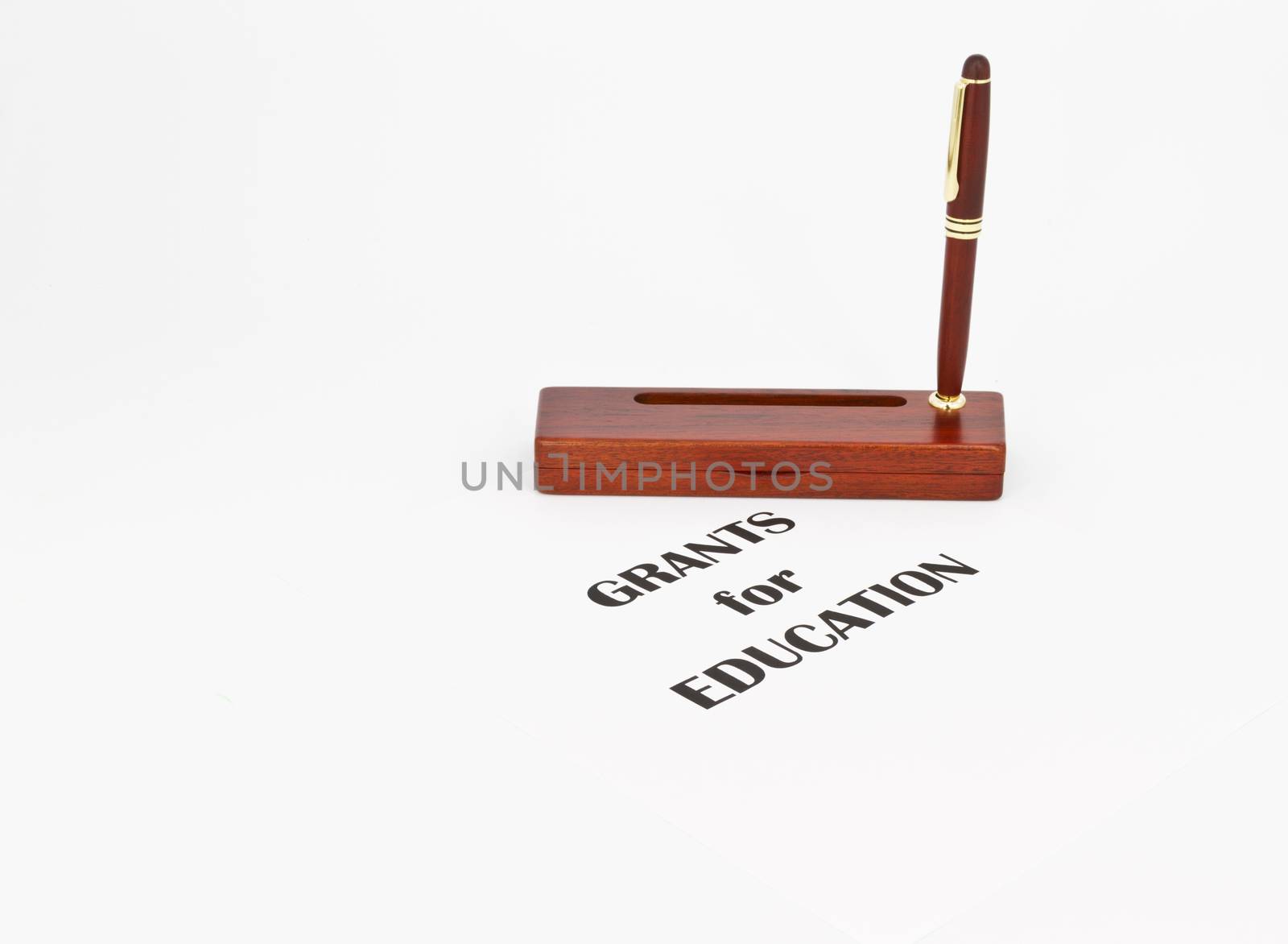 Pen in rosewood stand indicates writing and text directs to grants and proposals that can fund schools and educational costs, supplies, and projects. Copy space available around direct, still life metaphors of horizontal image.