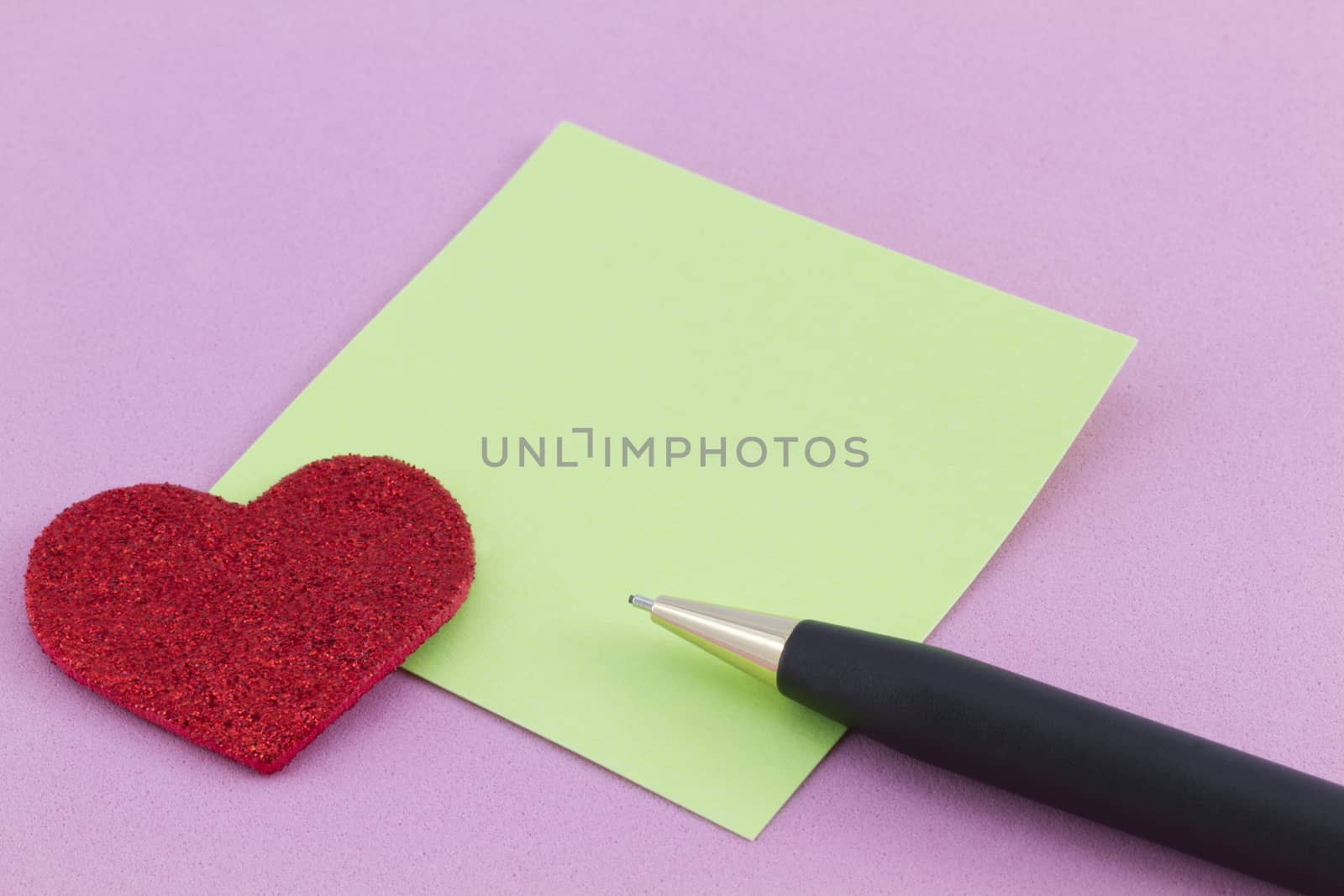 Sparkling red heart next to green note square with black pen on pink background. Copy space available.
