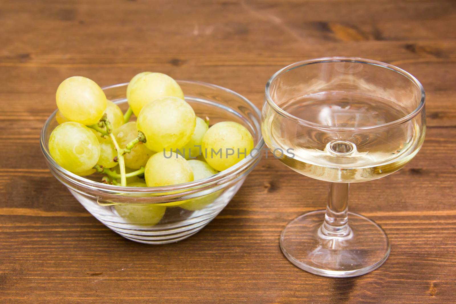 Glass of wine and grapes on bowl on wooden table