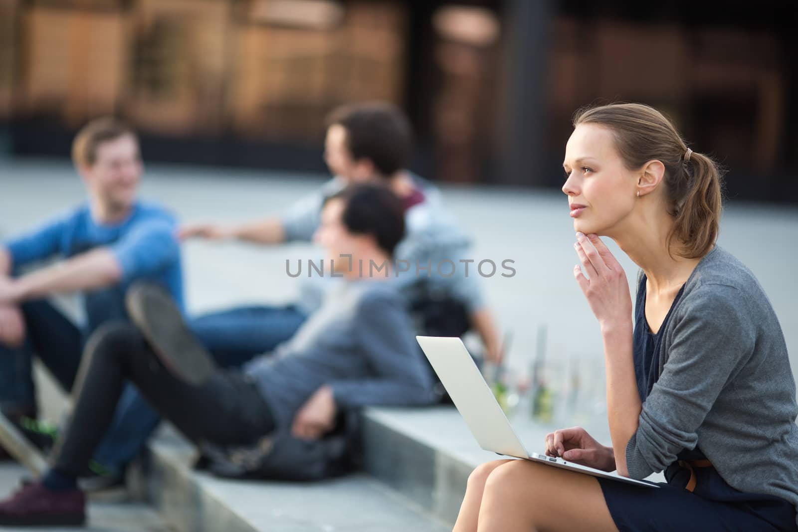 Portrait of a sleek young woman, using laptop computer, being pensive in urban/city context (shallow DOF; color toned image)