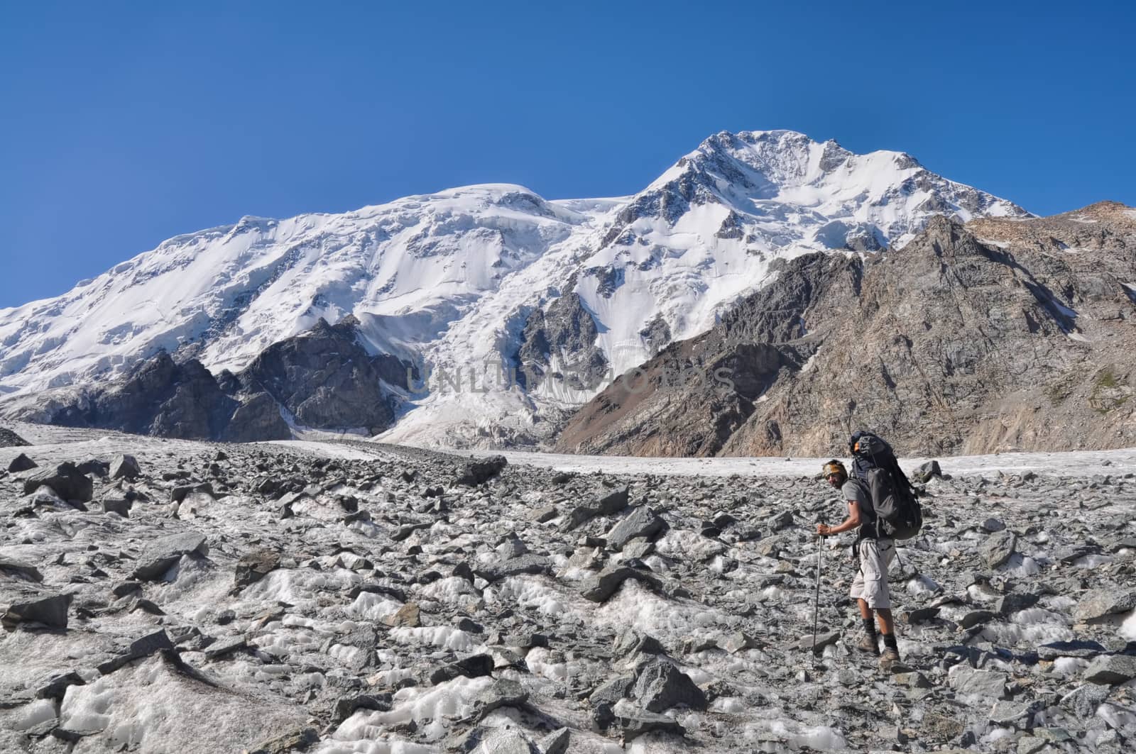 Hiker with backpack on glacier below snow-covered highest peaks in Tien-Shan mountain range in Kyrgyzstan