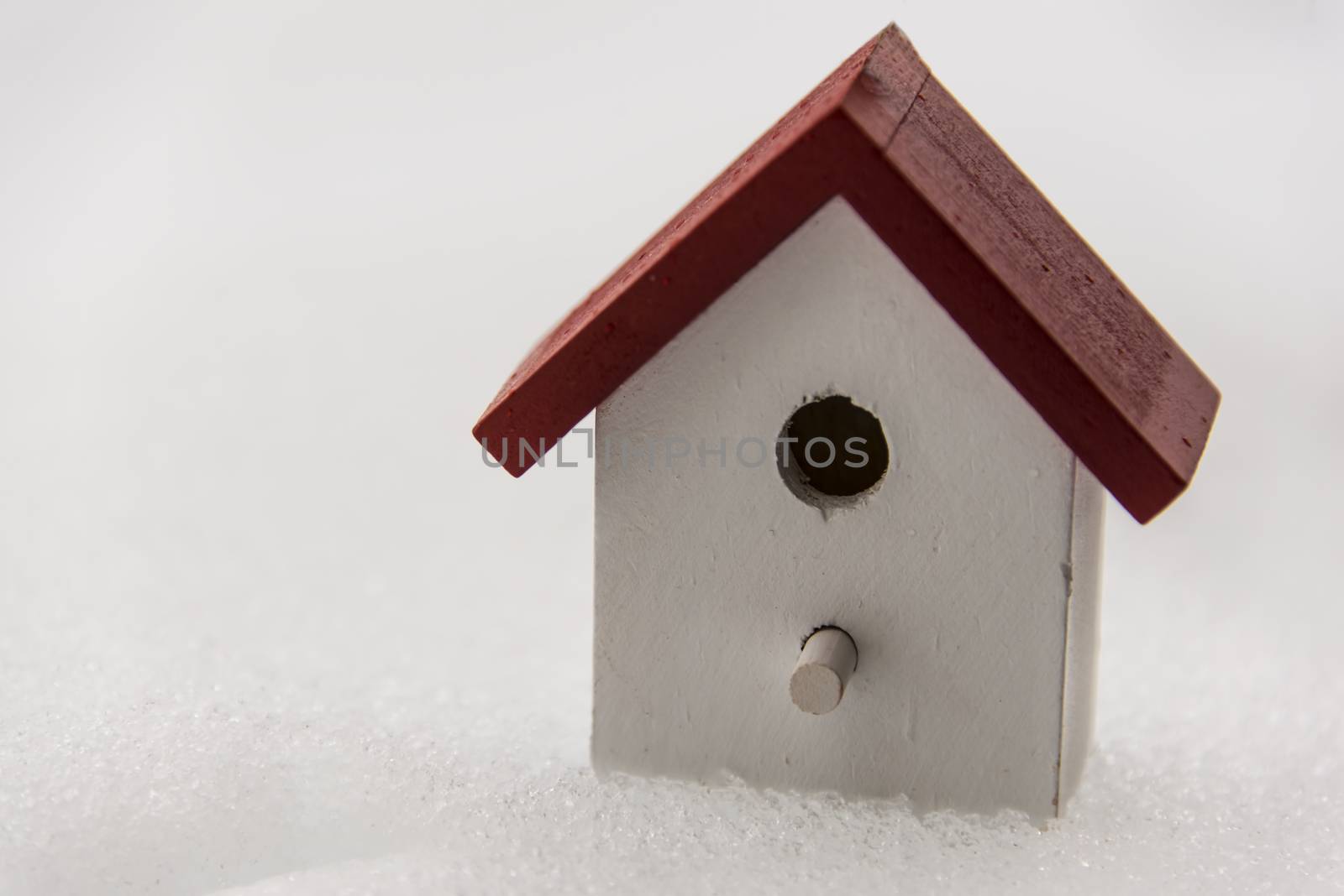 A small wooden bird house in red and white in the snow