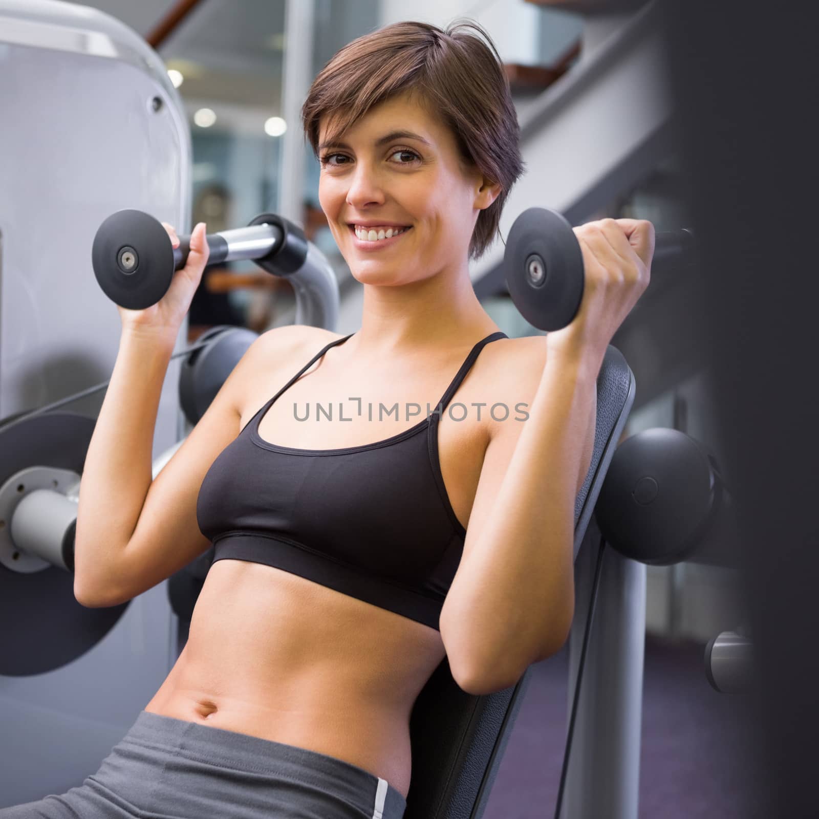 Smiling brunette using weights machine for arms at the gym