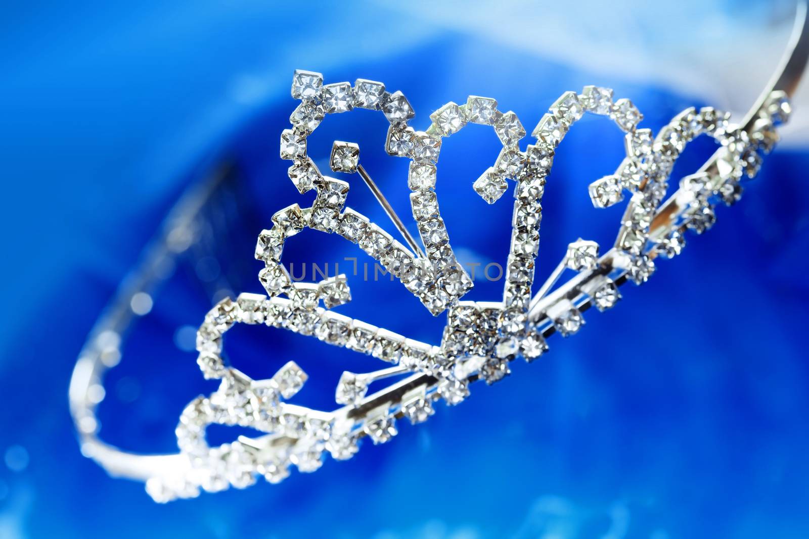 Close-up photo of the silver diadem with diamonds on a blue background with bokeh