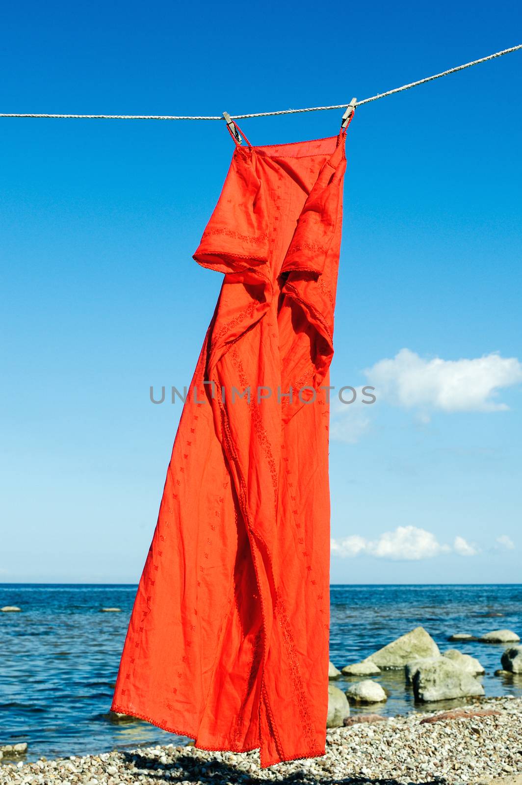 Red sundress hanging on a rope on the seashore
