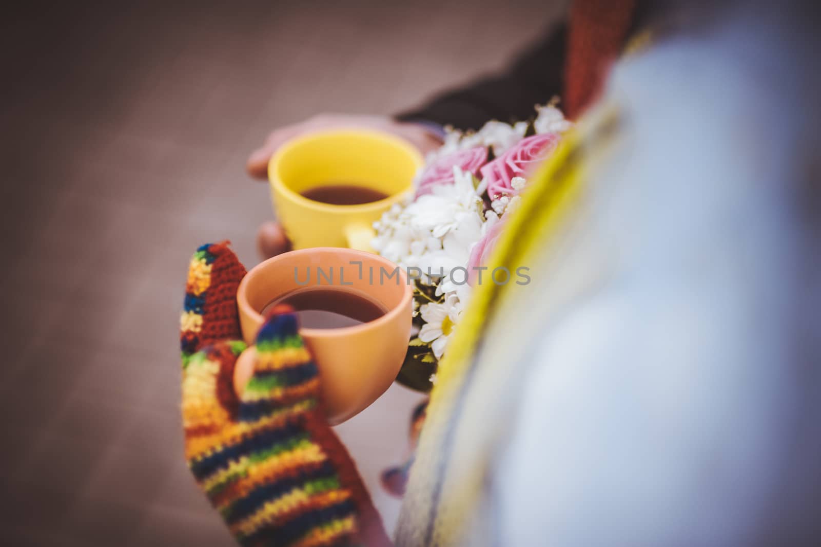 couple holding colorful cups of tea wearing mittens