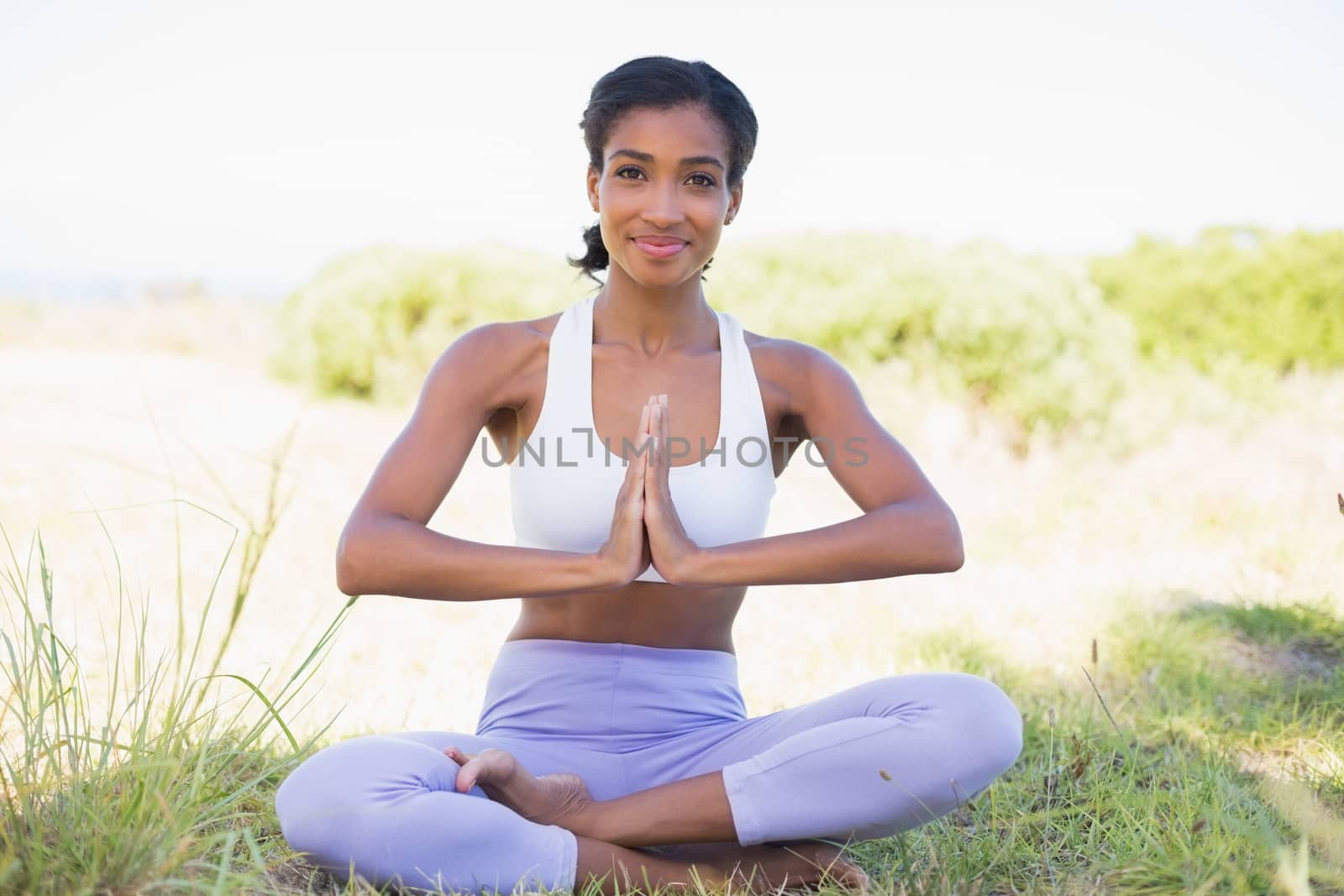 Fit woman sitting on grass in lotus pose smiling at camera on a sunny day in the countryside
