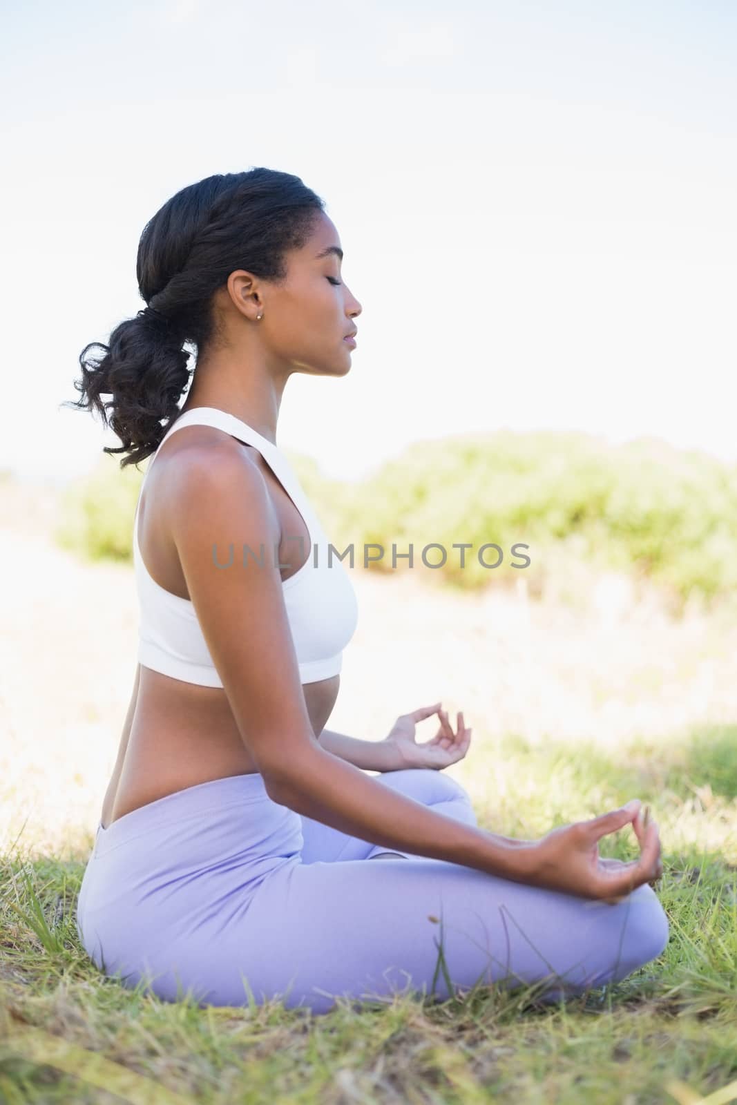 Fit woman sitting on grass in lotus pose with eyes closed on a sunny day in the countryside