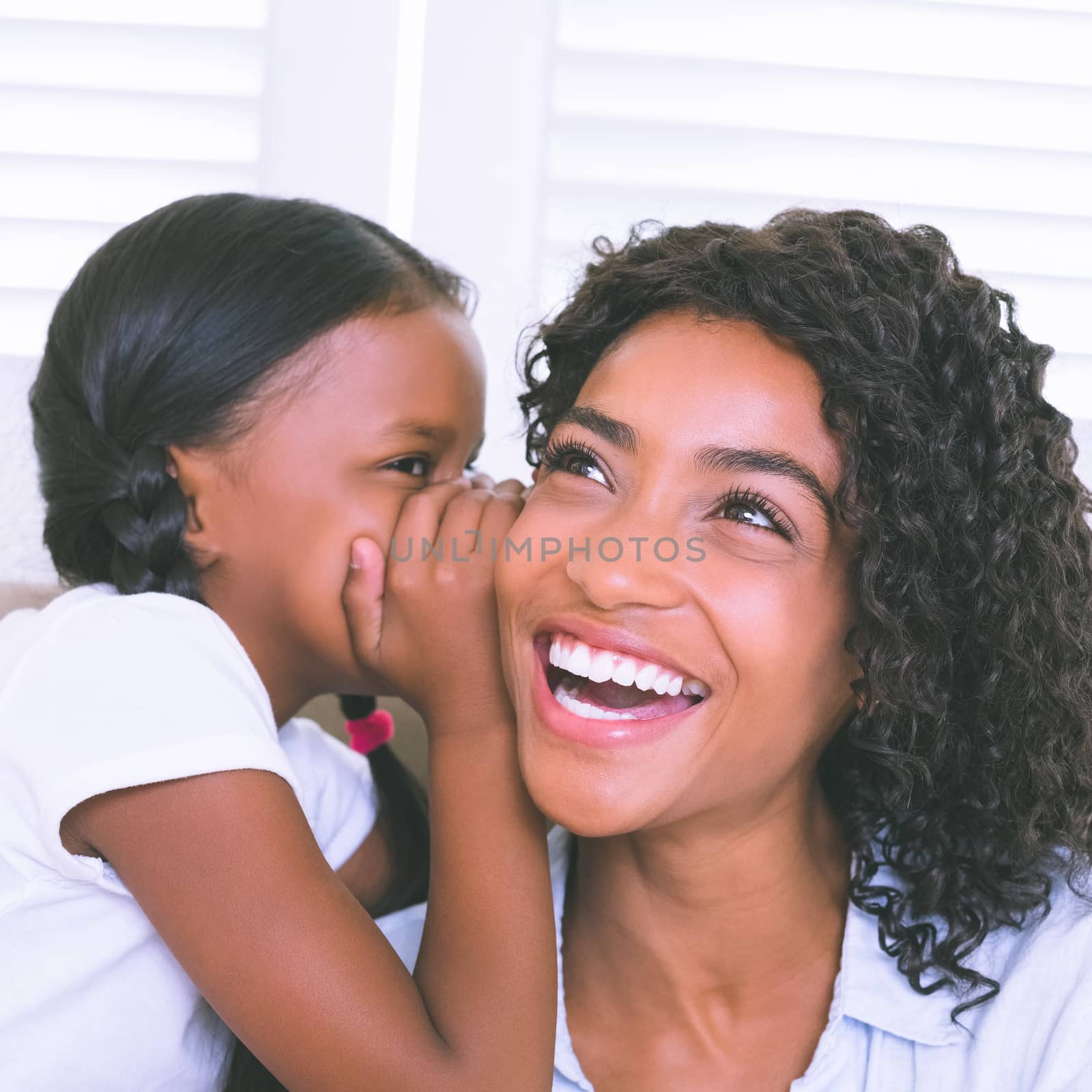 Pretty mother sitting on the couch with her daughter whispering a secret at home in the living room