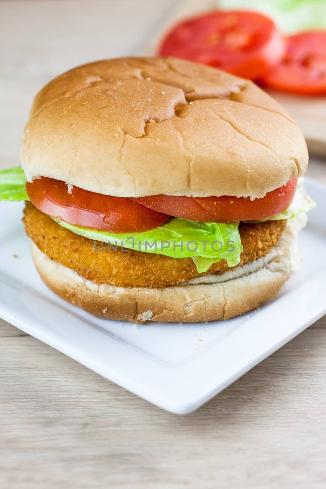 A chicken sandwich with fresh tomato and lettuce on a white plate.