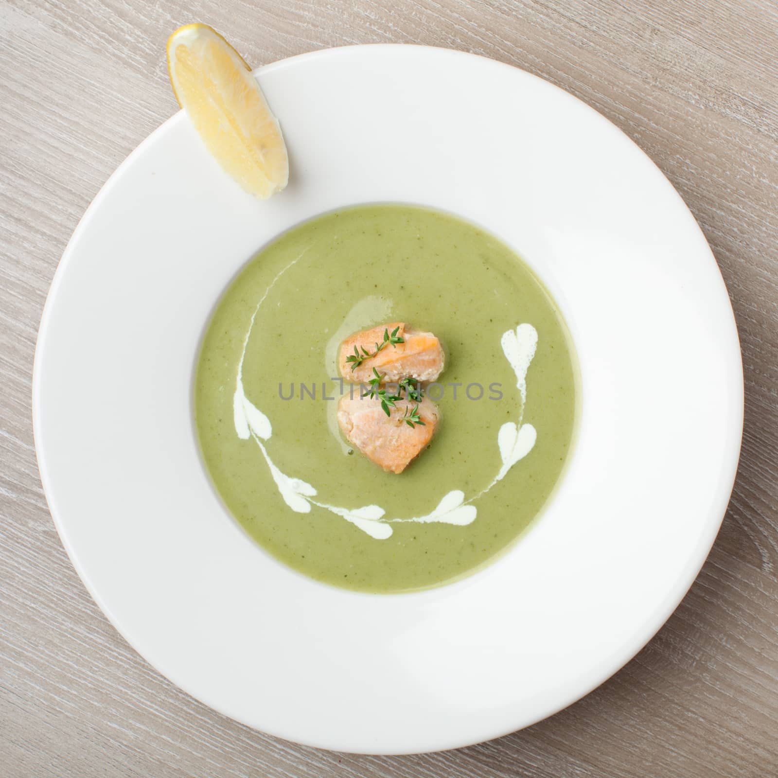 Green cabbage broccoli cream soup puree in white plate  served with  filleted salmon pieces , lemon and  theme