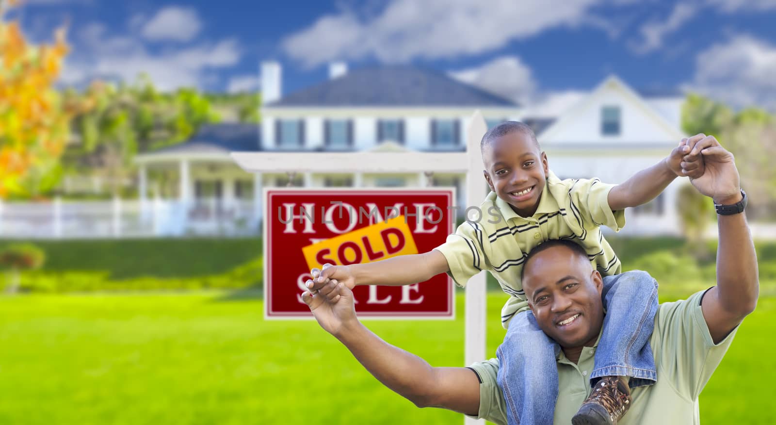 Happy African American Father and Son in Front of New Home and Sold Real Estate Sign.