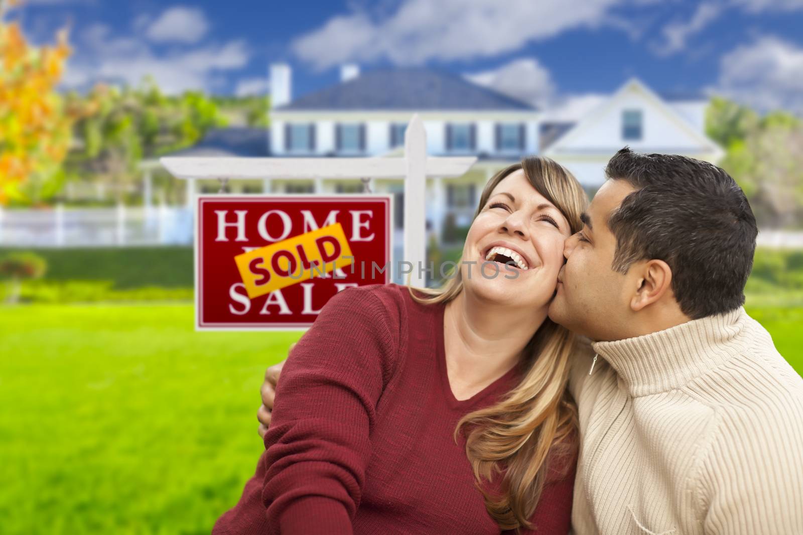 Happy Mixed Race Couple in Front of Sold Real Estate Sign.